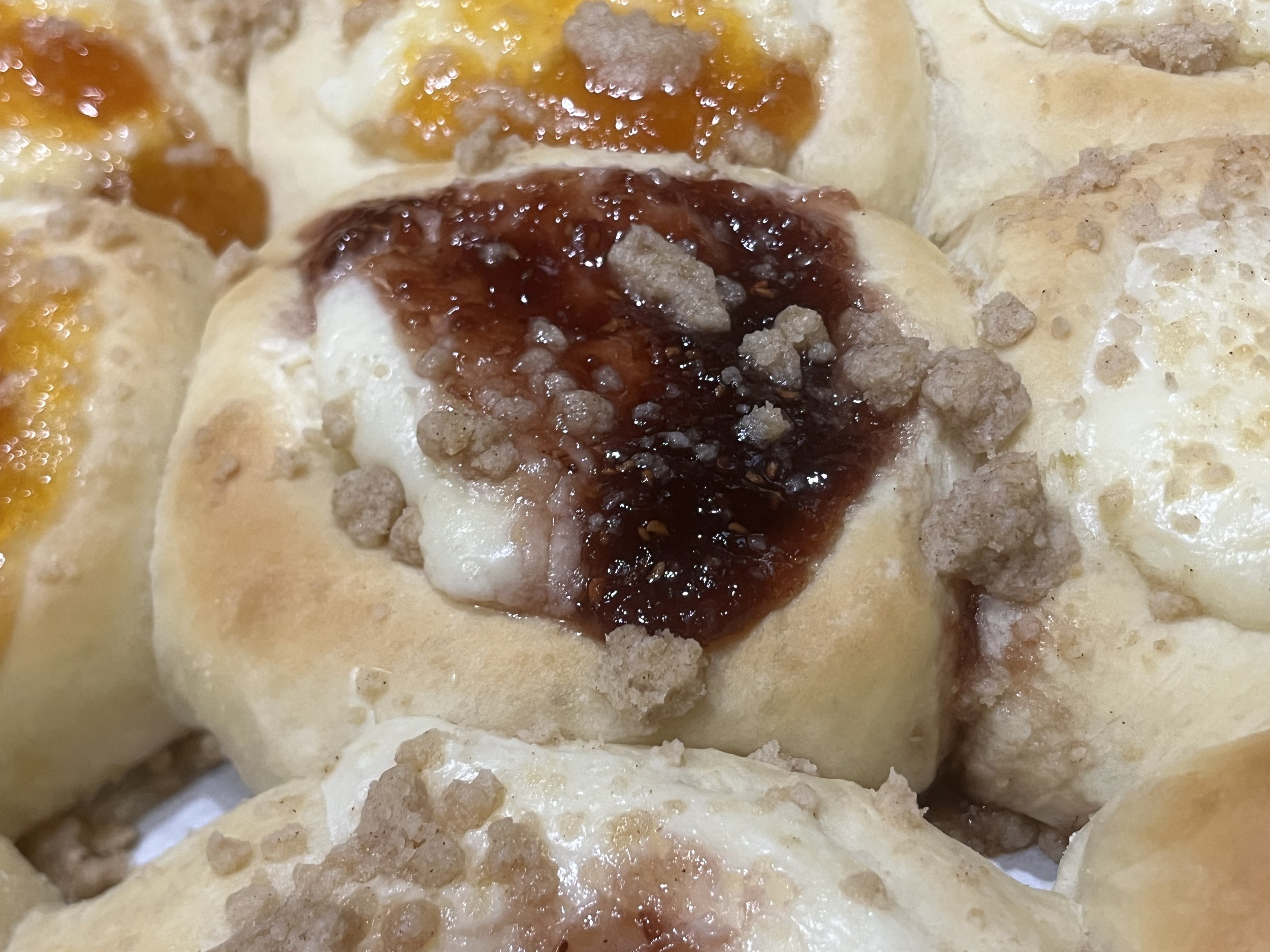 Close-up of cinnamon rolls topped with brown sugar, with some rolls having orange or yellow icing and glaze.