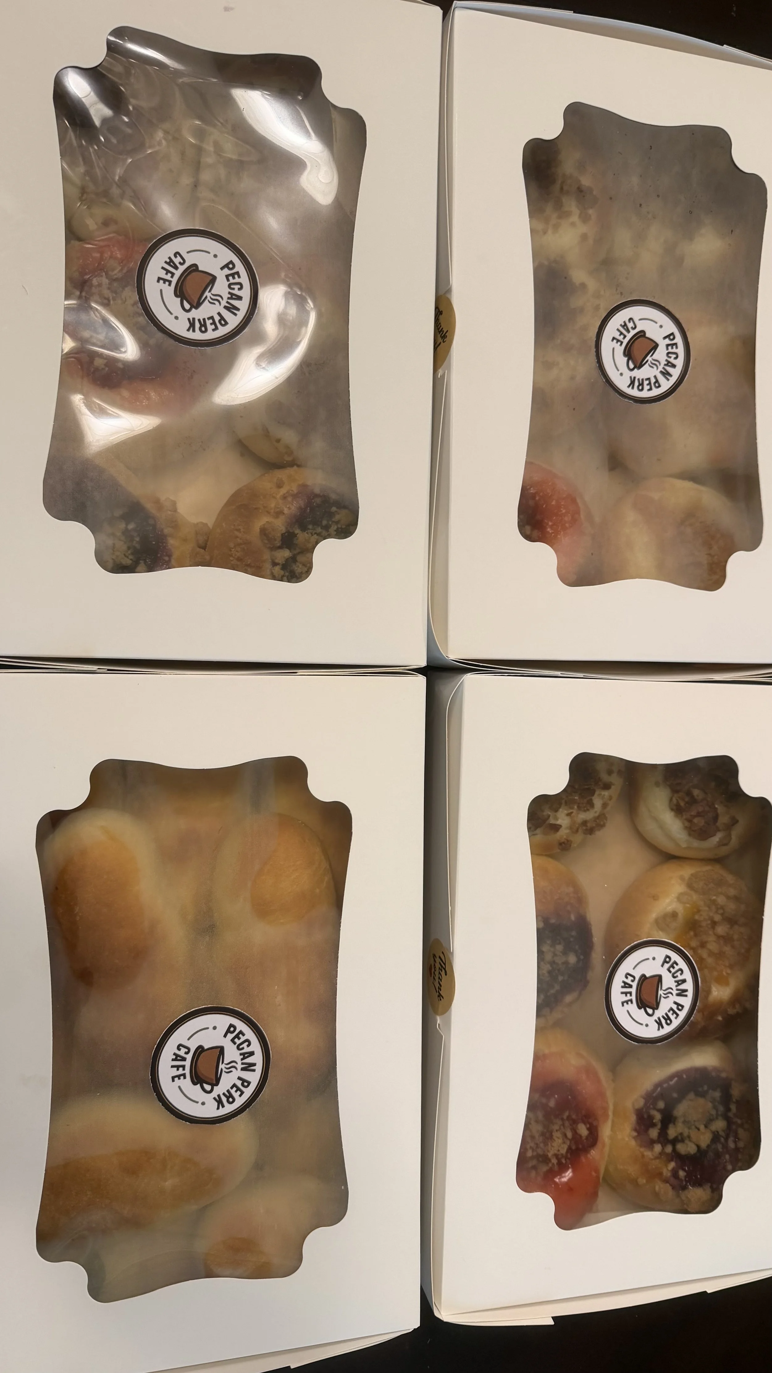 Four white boxes with clear windows showing assorted cookies inside, each box labeled with a round sticker featuring a coffee cup and the text 'Pecan Pie Cafe'.