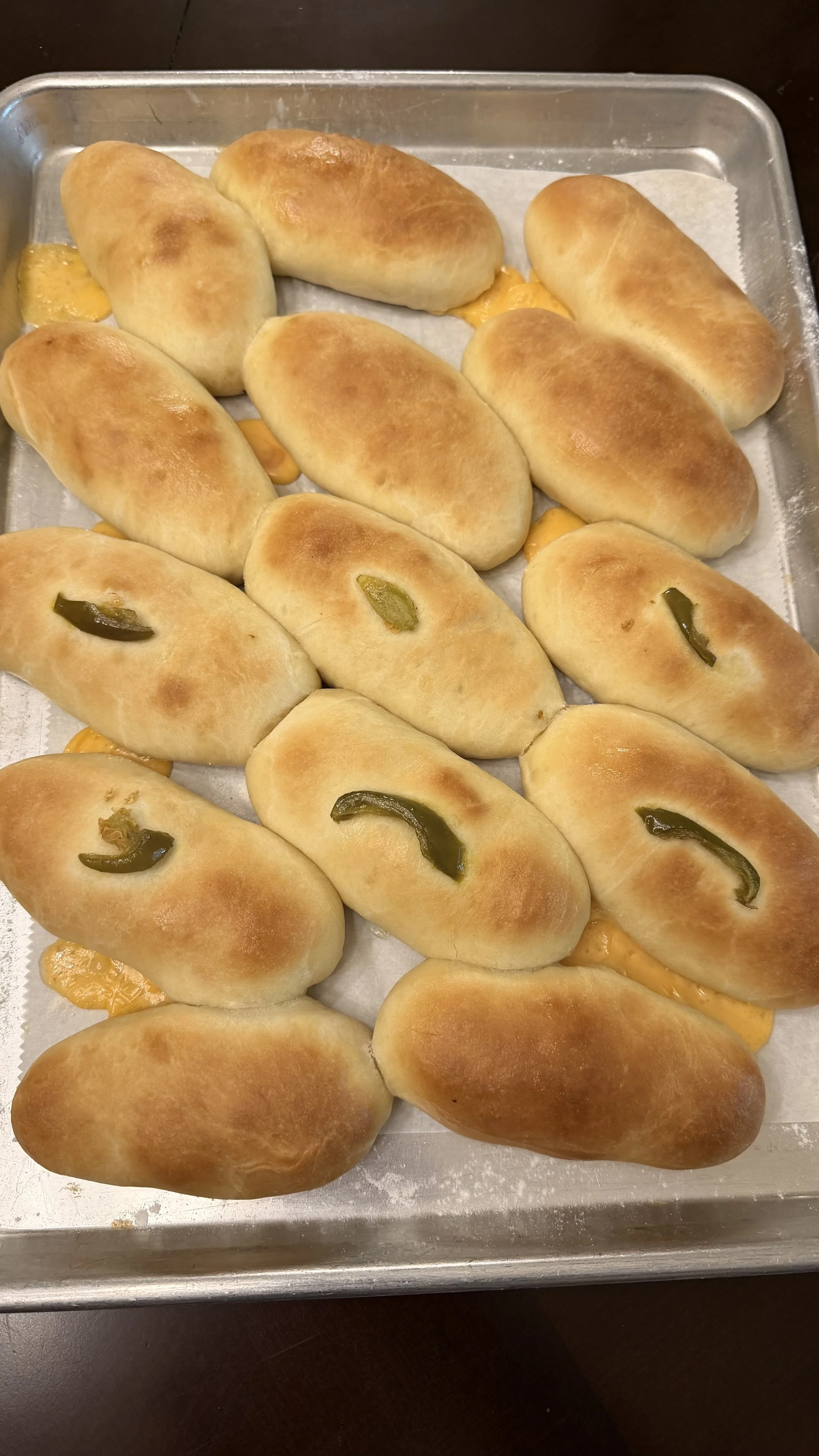 Baked bread rolls topped with jalapeño slices on a baking sheet.