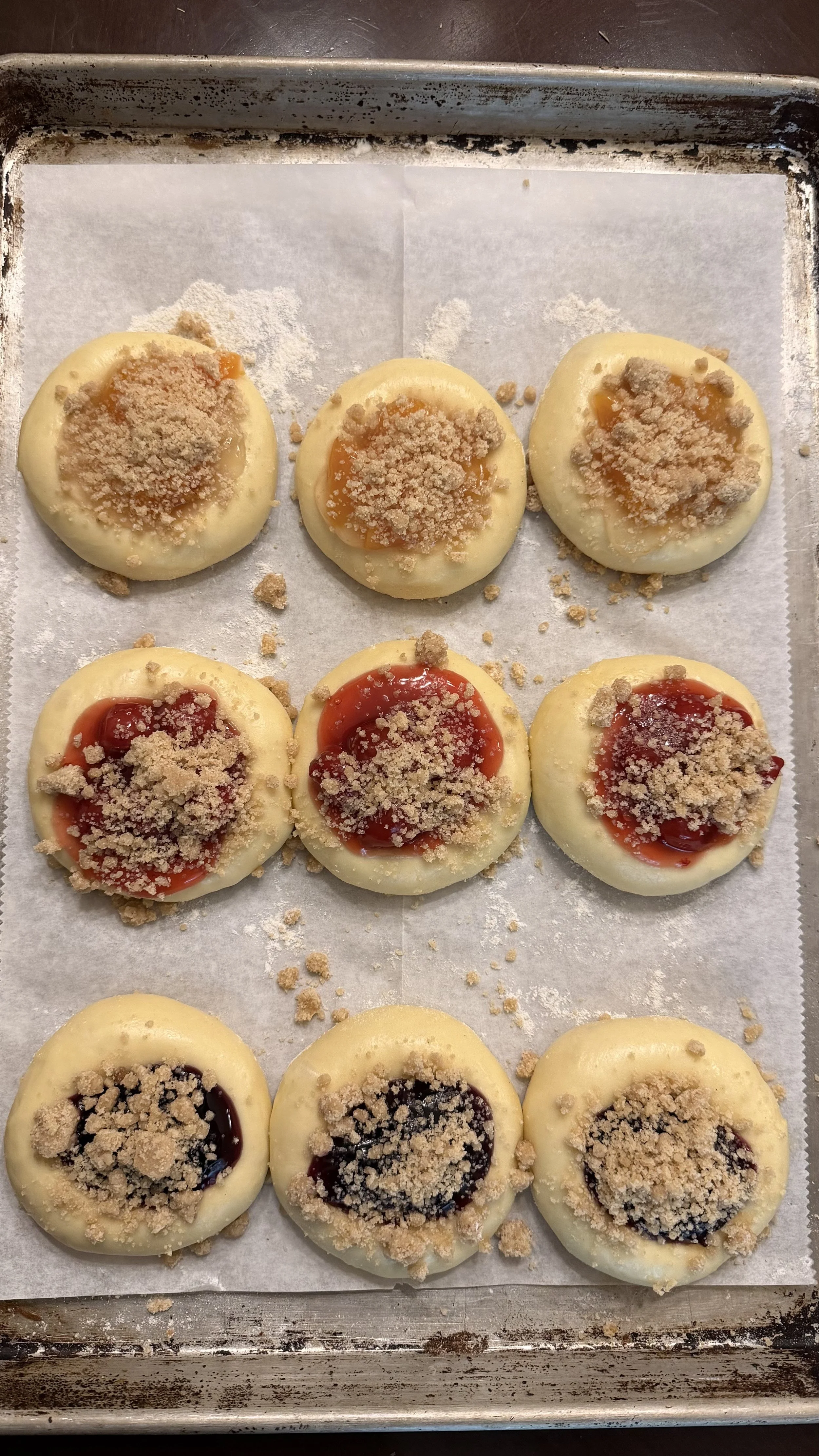 Baked round cookies with various fruit jams and graham cracker crumbs on top, arranged on a baking sheet lined with parchment paper.