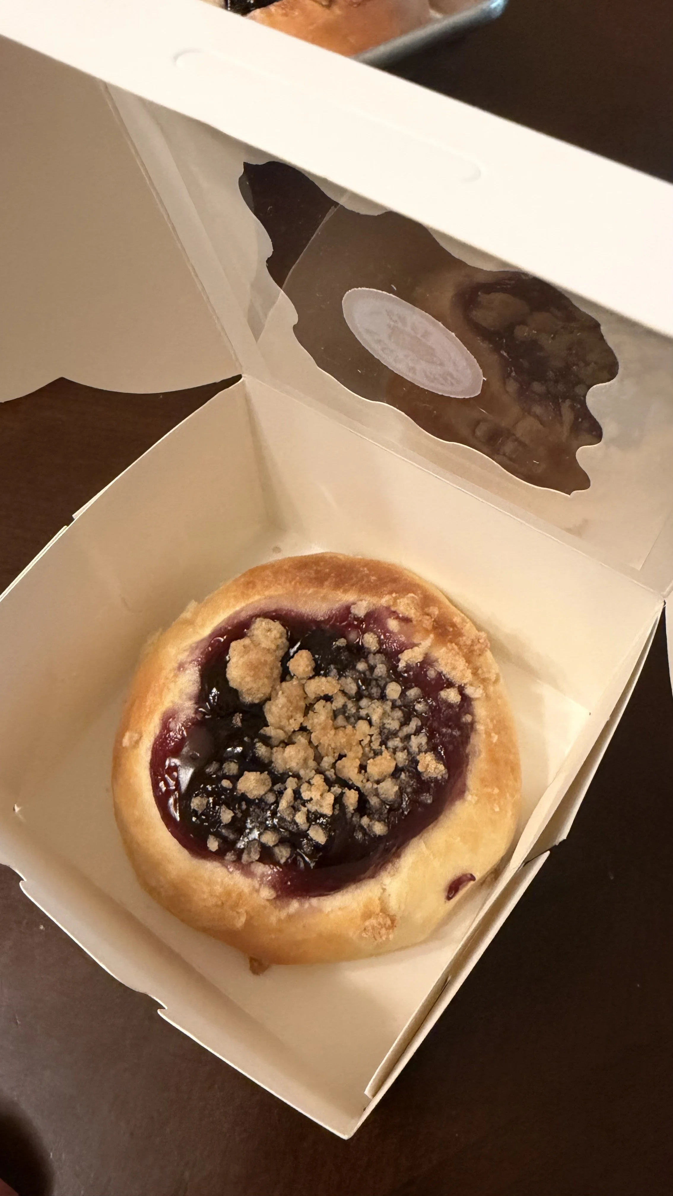 A round pastry with a berry filling and crumb topping inside a white bakery box.