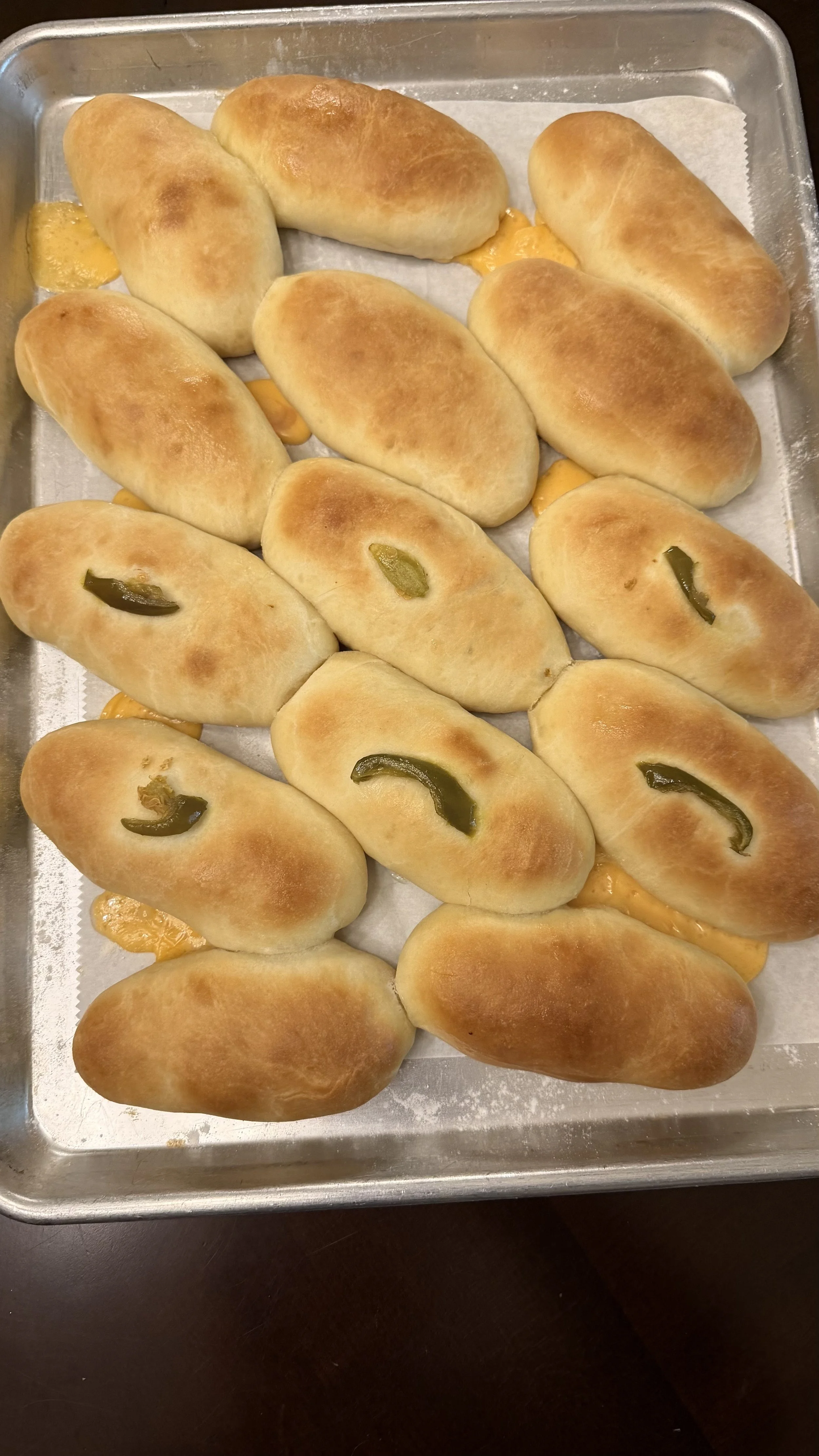 Tray of freshly baked hot dog buns, some with jalapeño slices on top, and some cheese-filled buns underneath.