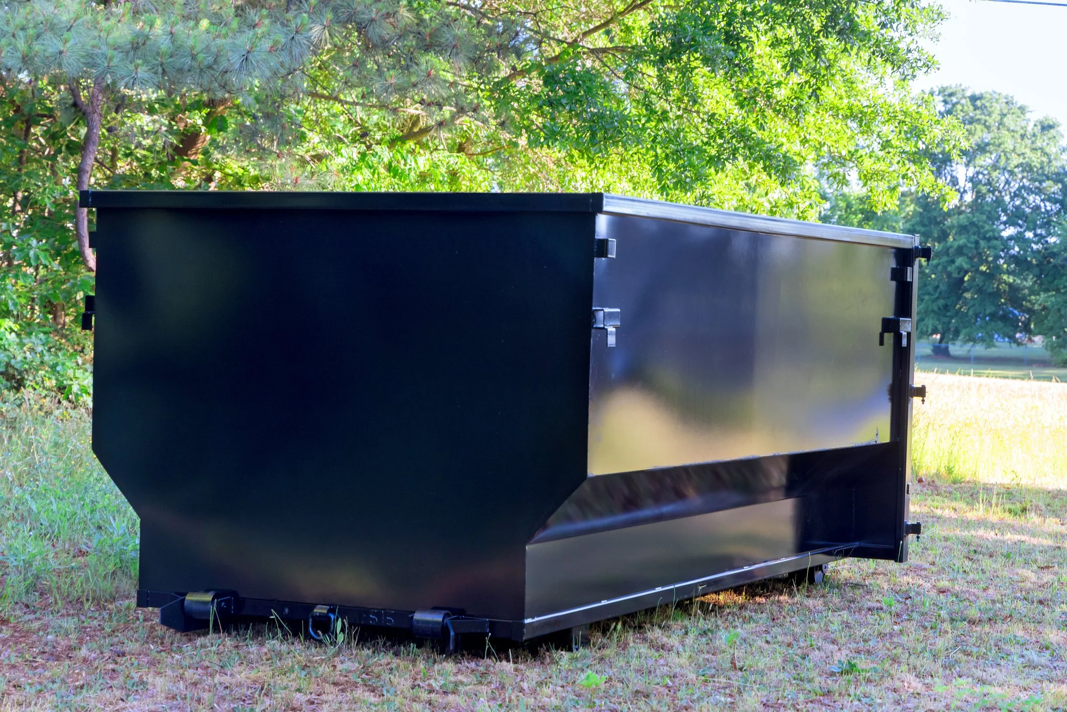 Large black metal storage container placed outdoors on a grassy area surrounded by trees and greenery.