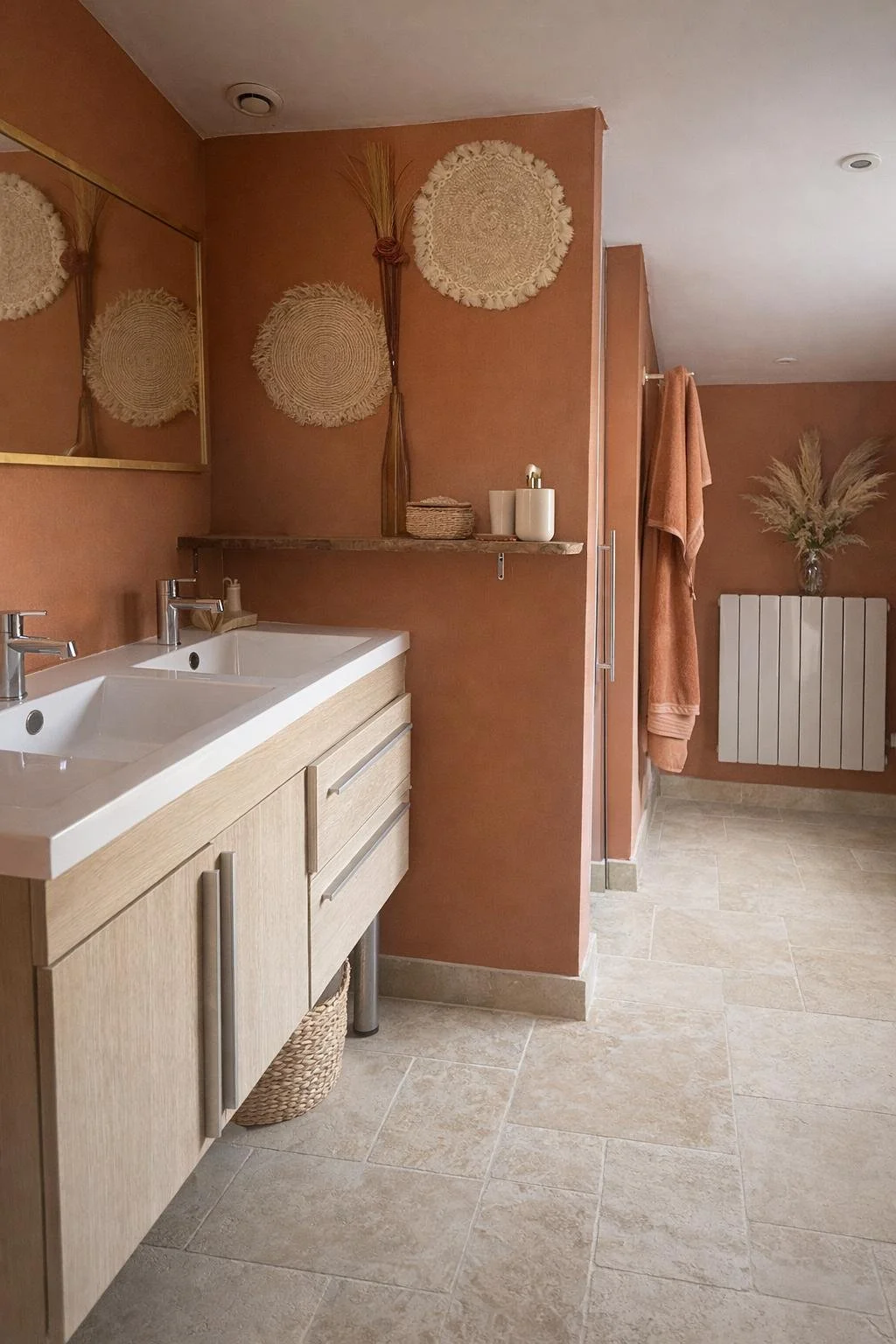 Salle de bain avec un lavabo double en bois clair, décoration naturelle avec paniers, tapis tissé, et plantes séchées, murs de couleur terre cuite