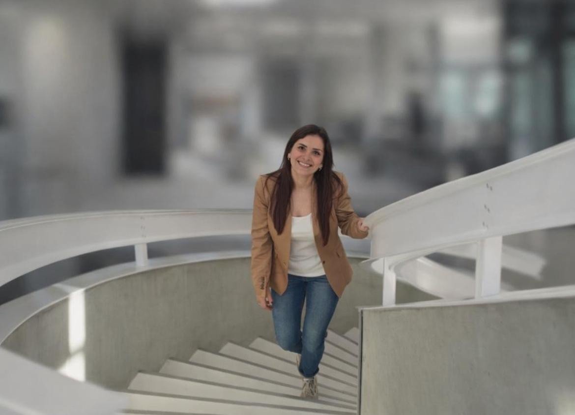 Une femme souriante descend un escalier tournant en intérieur.
