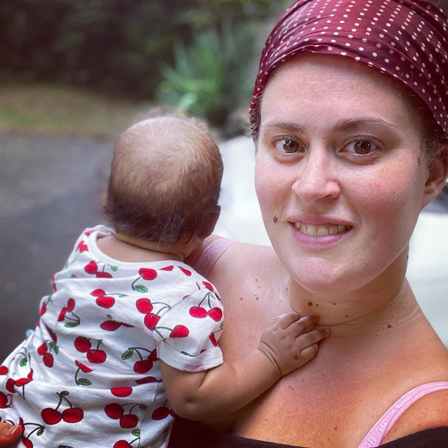 Una donna con un foulard rossa con pois bianchi tiene in braccio un bambino con una maglietta con ciliegie stampate. Donna lavoratrice in maternità. Esperienza di crescita personale professionale, sviluppo competenze trasversali utili sul lavoro.