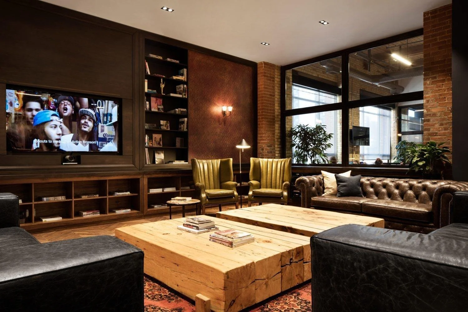 Cozy living room with brick and wood accents, leather sofas, vintage armchairs, a large wooden coffee table, and a TV on the wall.