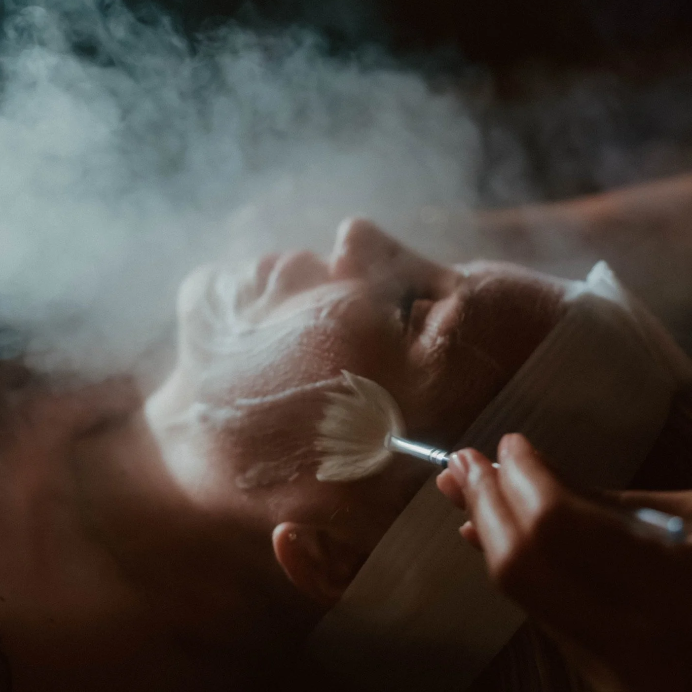 Patient lying down with their eyes closed, receiving a facial massage with a brush, surrounded by mist at Maven Haus medspa.