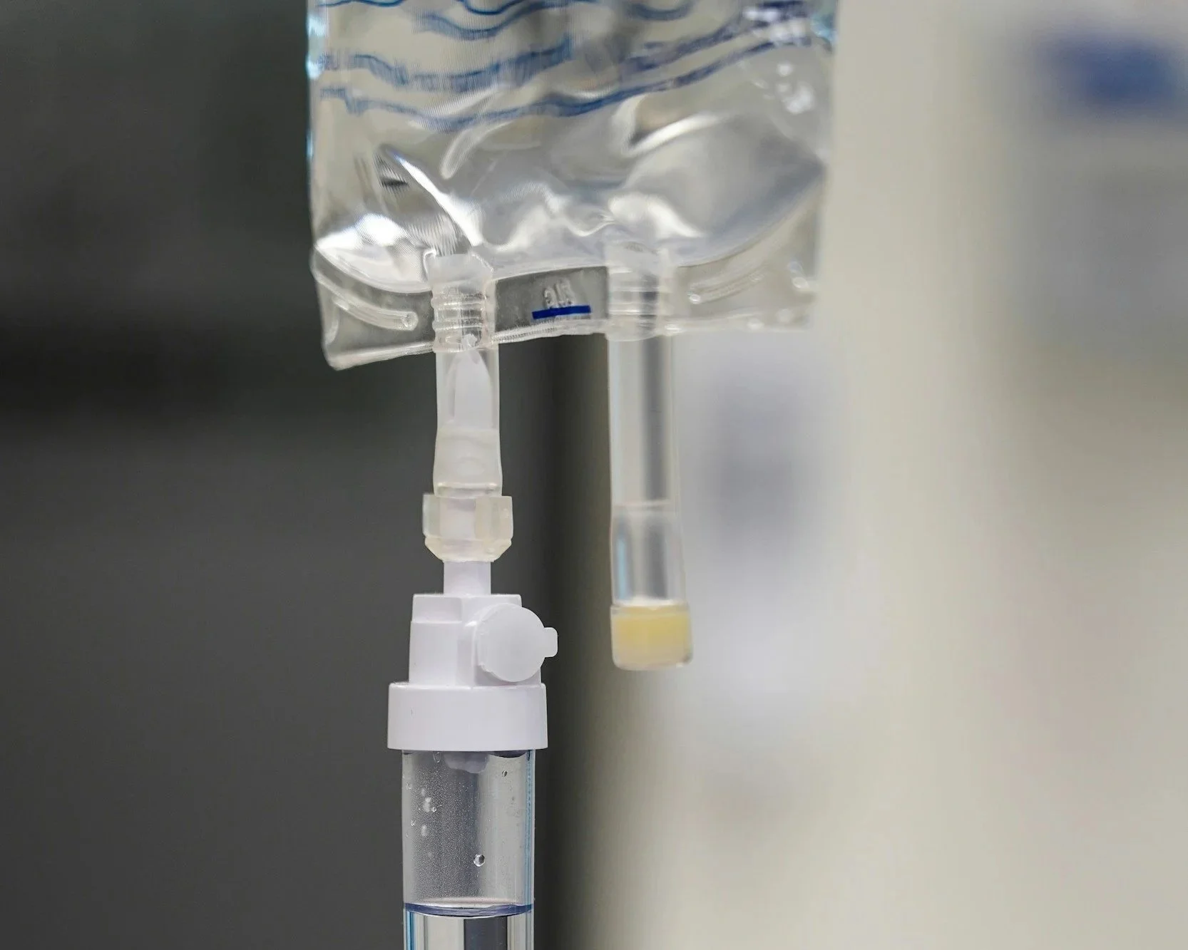A close-up of a medical intravenous (IV) drip with a clear fluid bag and a sterile tube connected to a patient's IV line.