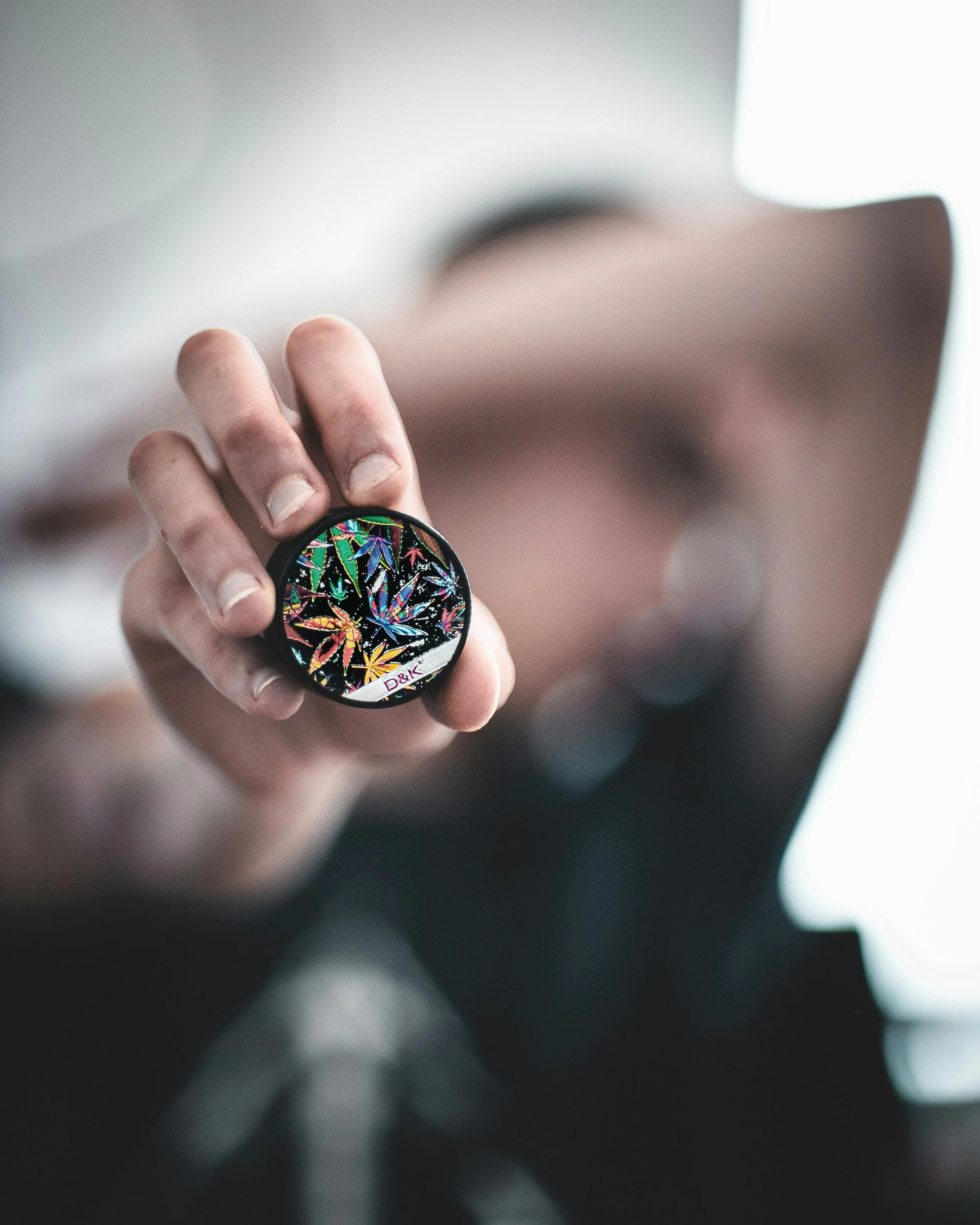 Une personne tient un pinceau de maquillage avec un motif coloré de feuilles de cannabis, flou en arrière-plan.