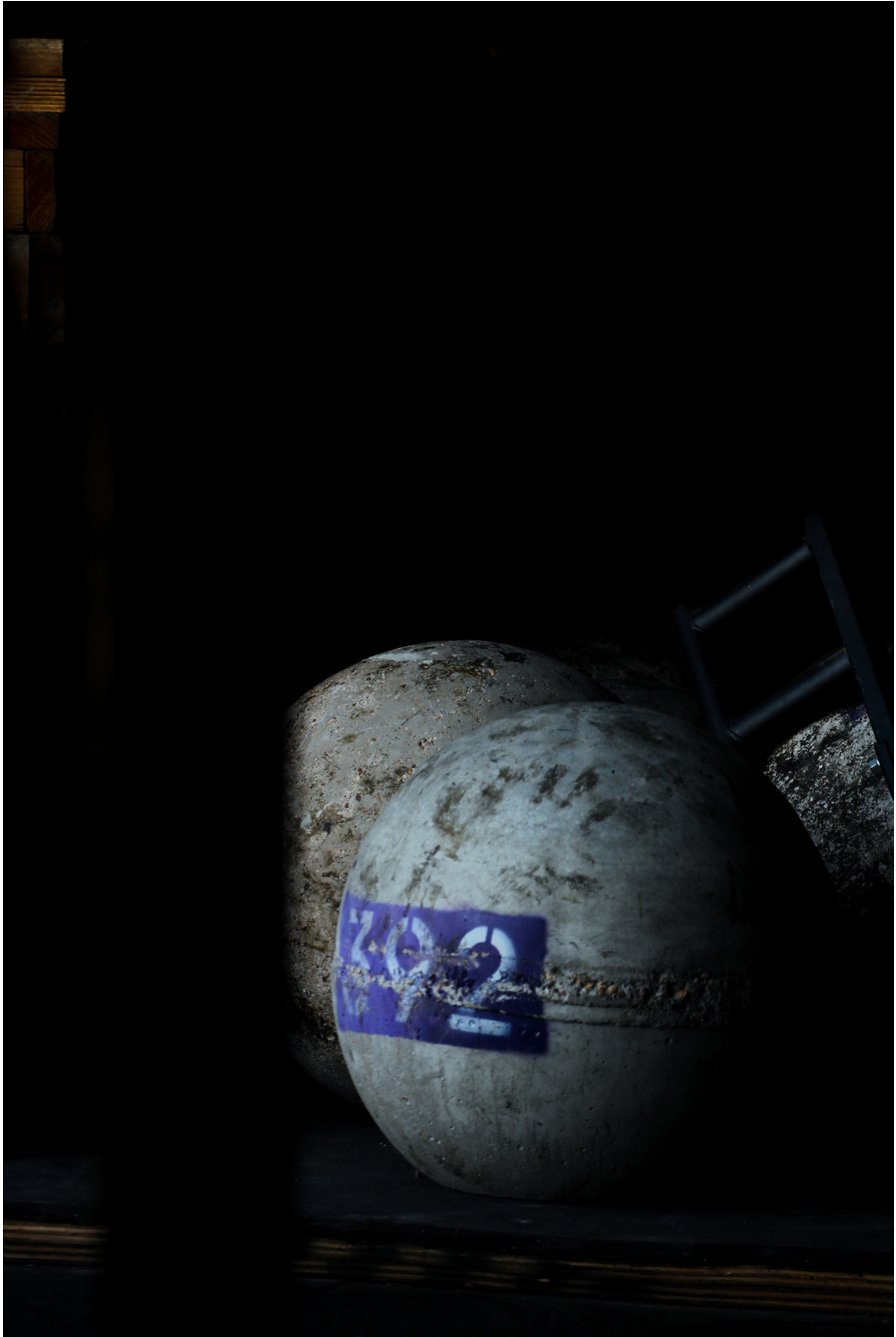 Two worn-out concrete buoys with a purple and white sticker, lying on the ground in a dark environment, with a black chair tilted in the background.