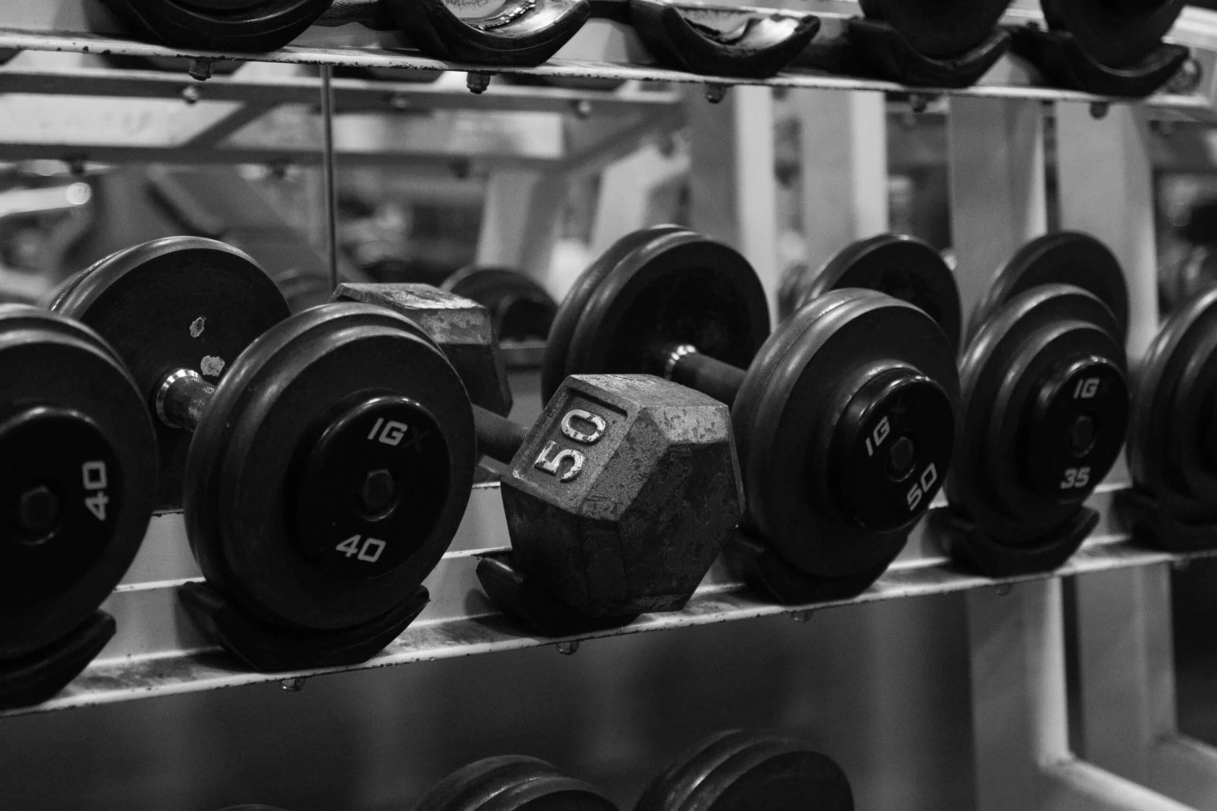Black and gray dumbbells on a rack in a gym, with one 50-pound dumbbell in the center.