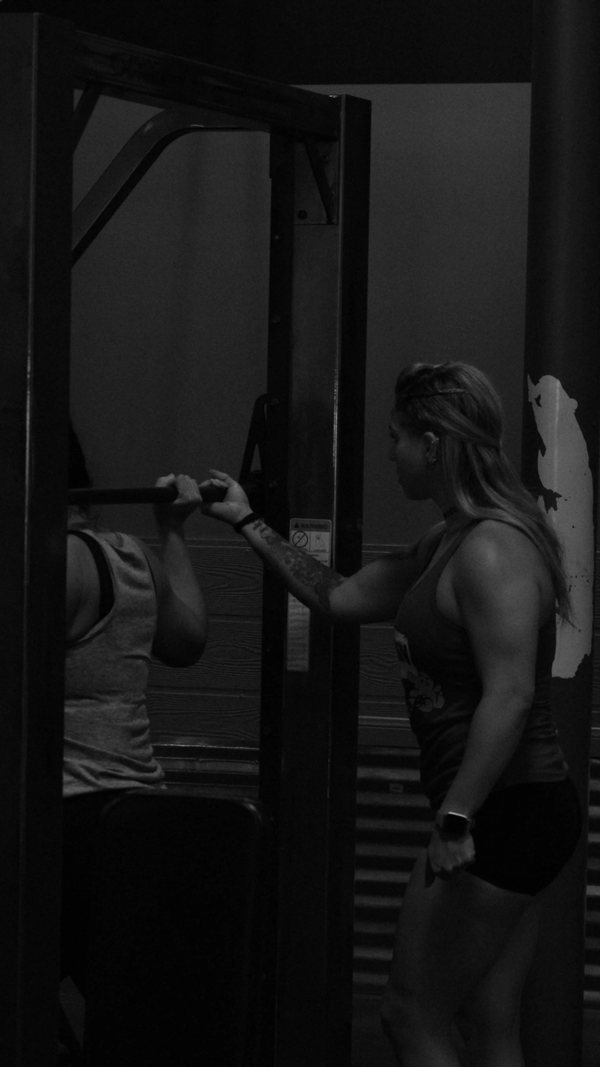A woman assisting a person with weightlifting in a gym.