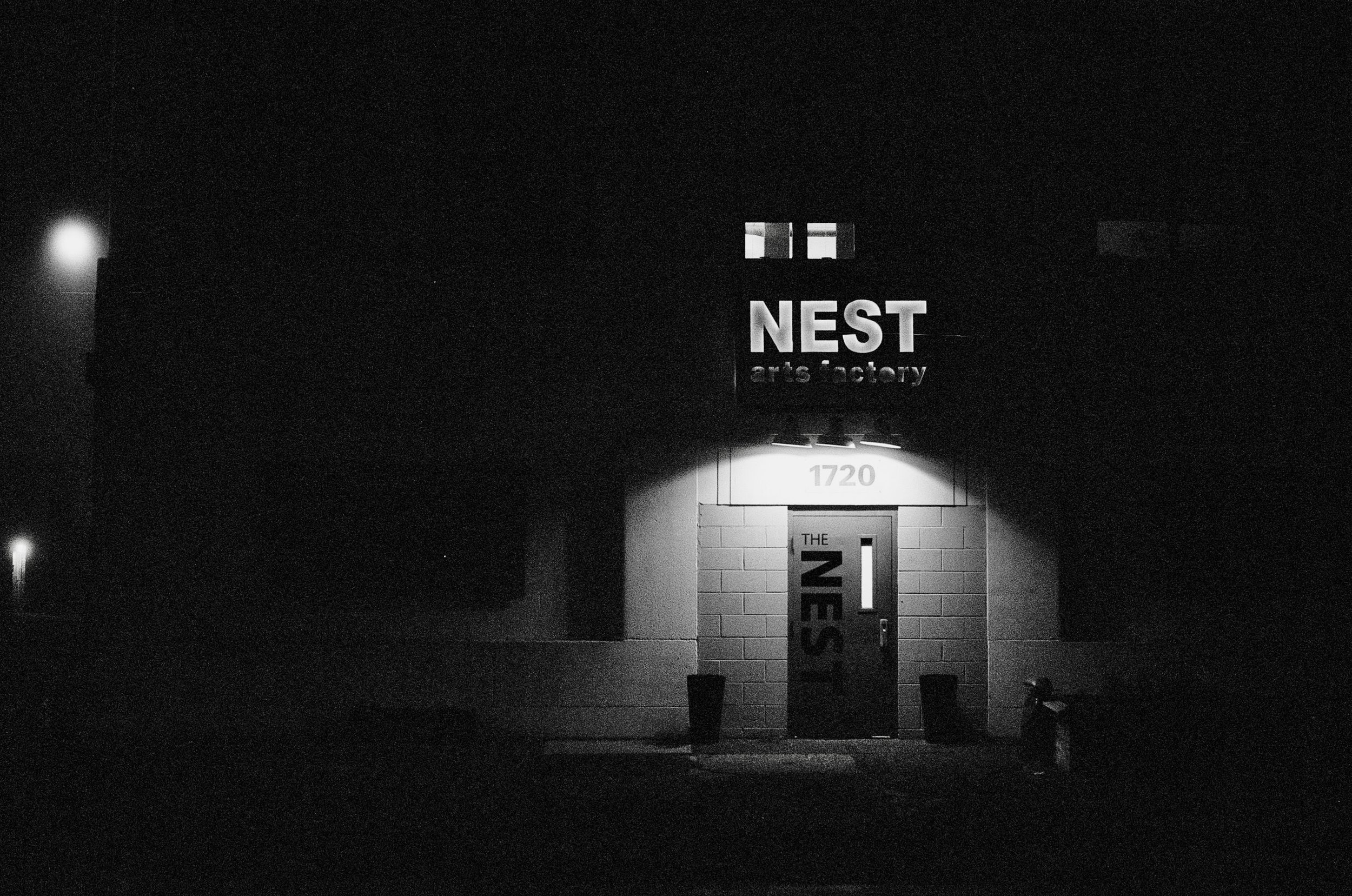 Night view of the NEST Arts Factory building with illuminated sign, door, and street number 1720.