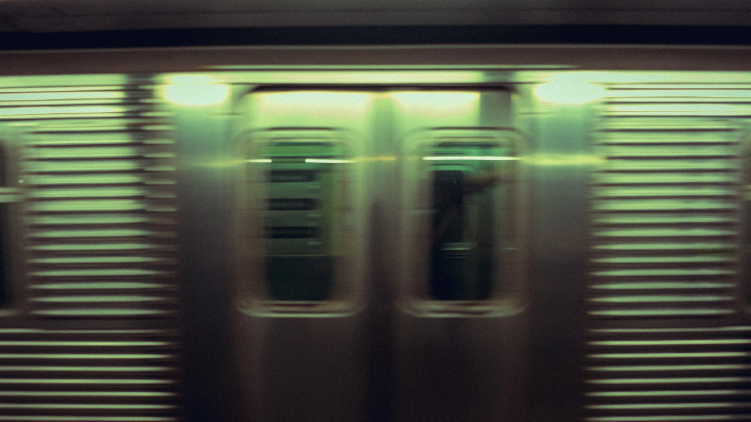 Blurred image of a moving train door with reflective metal sides and horizontal lines.