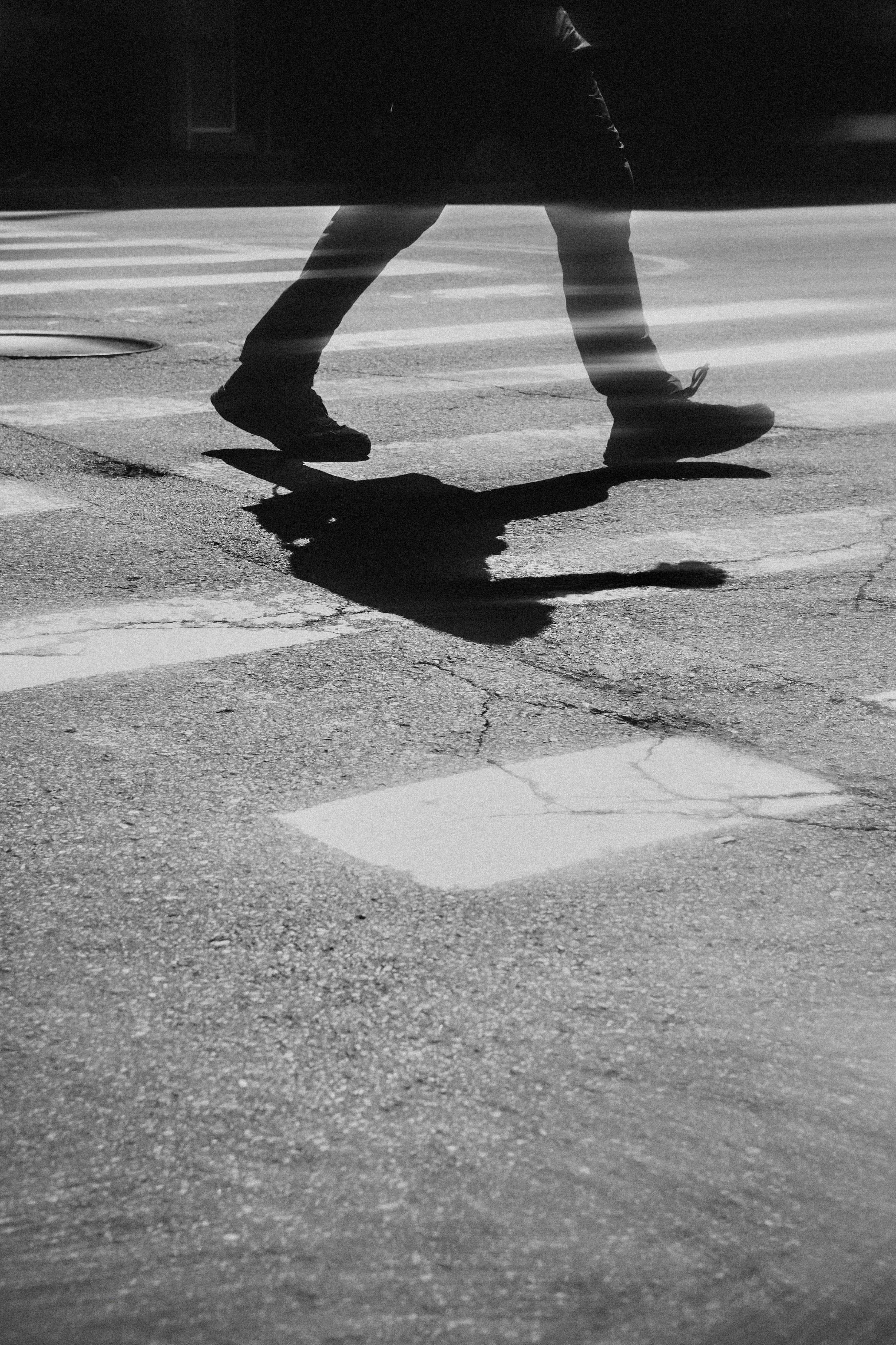 Shadow of a person walking on a crosswalk, reflected on the wet pavement, captured in black and white.