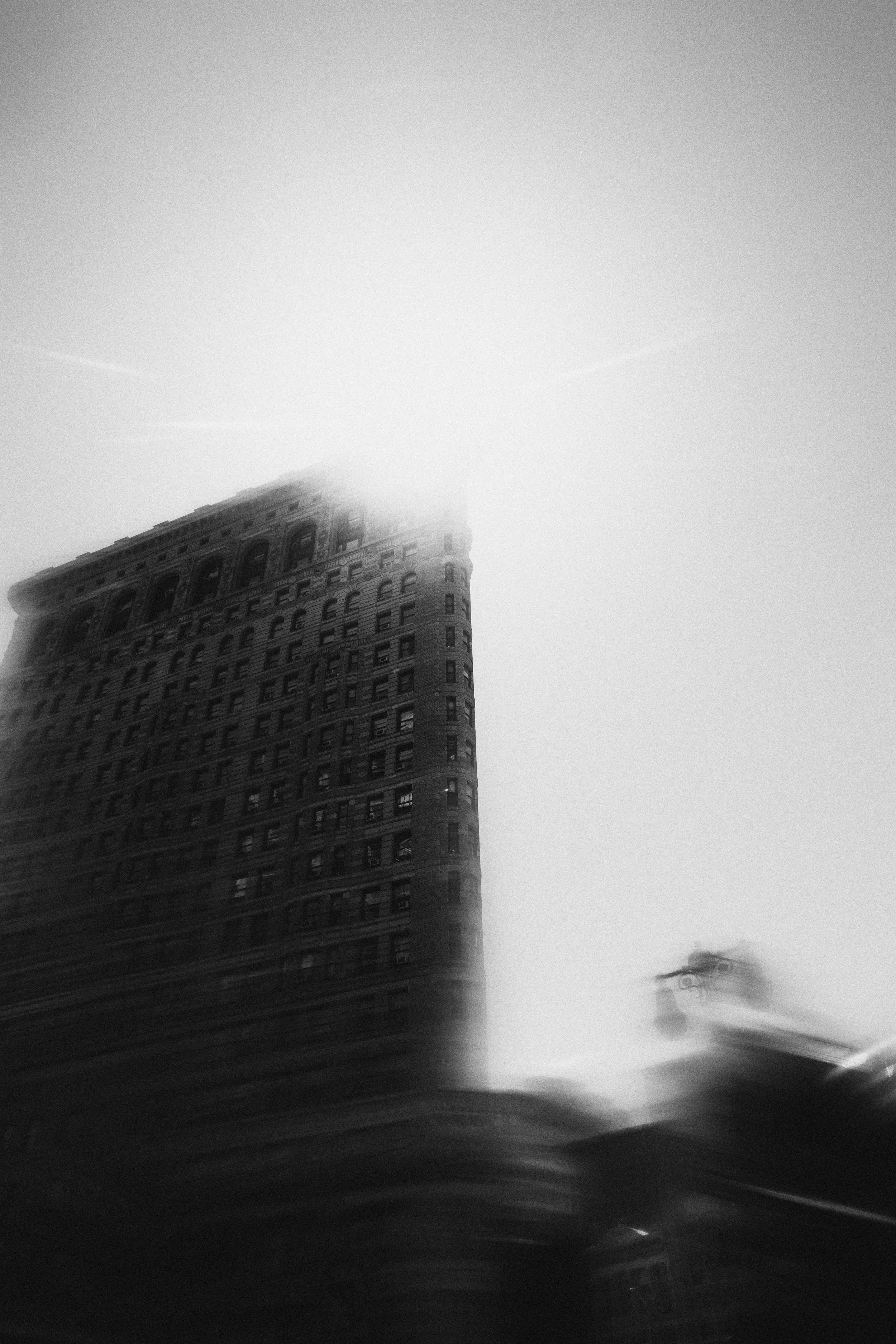 A tall, dark building with many windows, partially obscured by fog or mist, with a bright sky above.