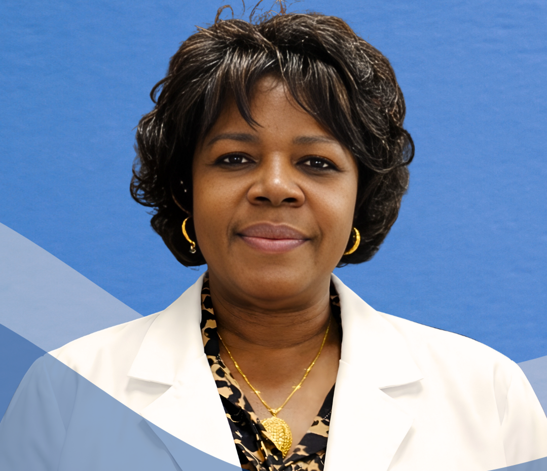 A middle-aged African American woman wearing a white lab coat, leopard print blouse, gold jewelry, with short curly hair, standing against a blue background.