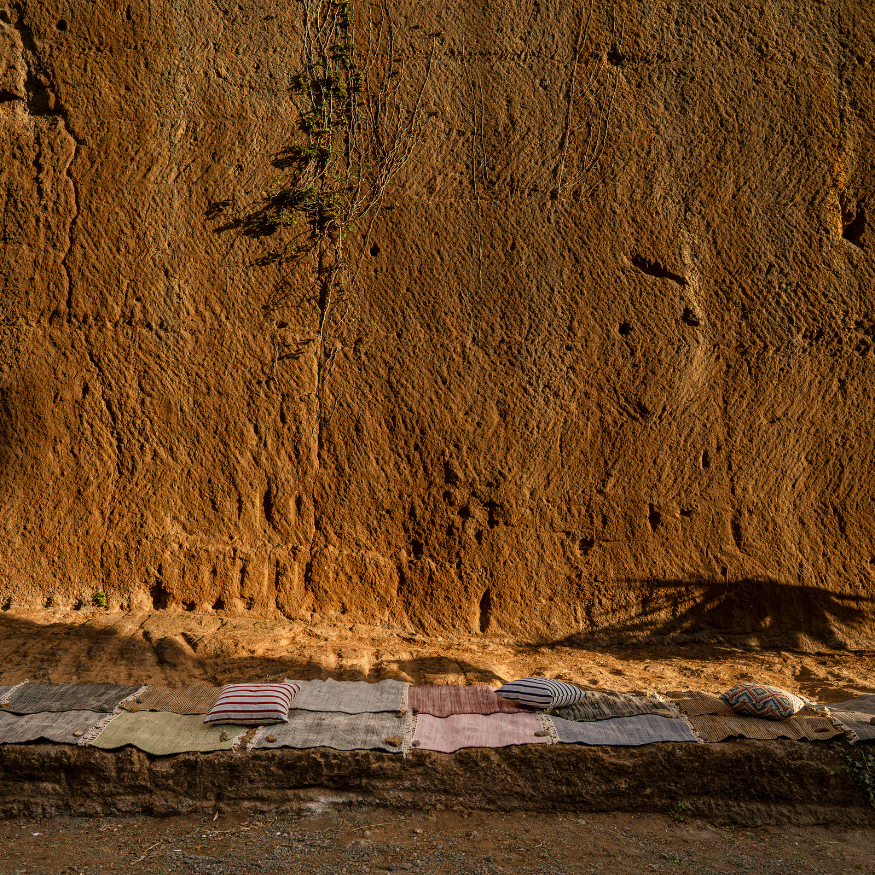 Sedile di pietra con cuscini su una superficie di mattoni, davanti a una parete di tufo chiamata Latomia di salone.