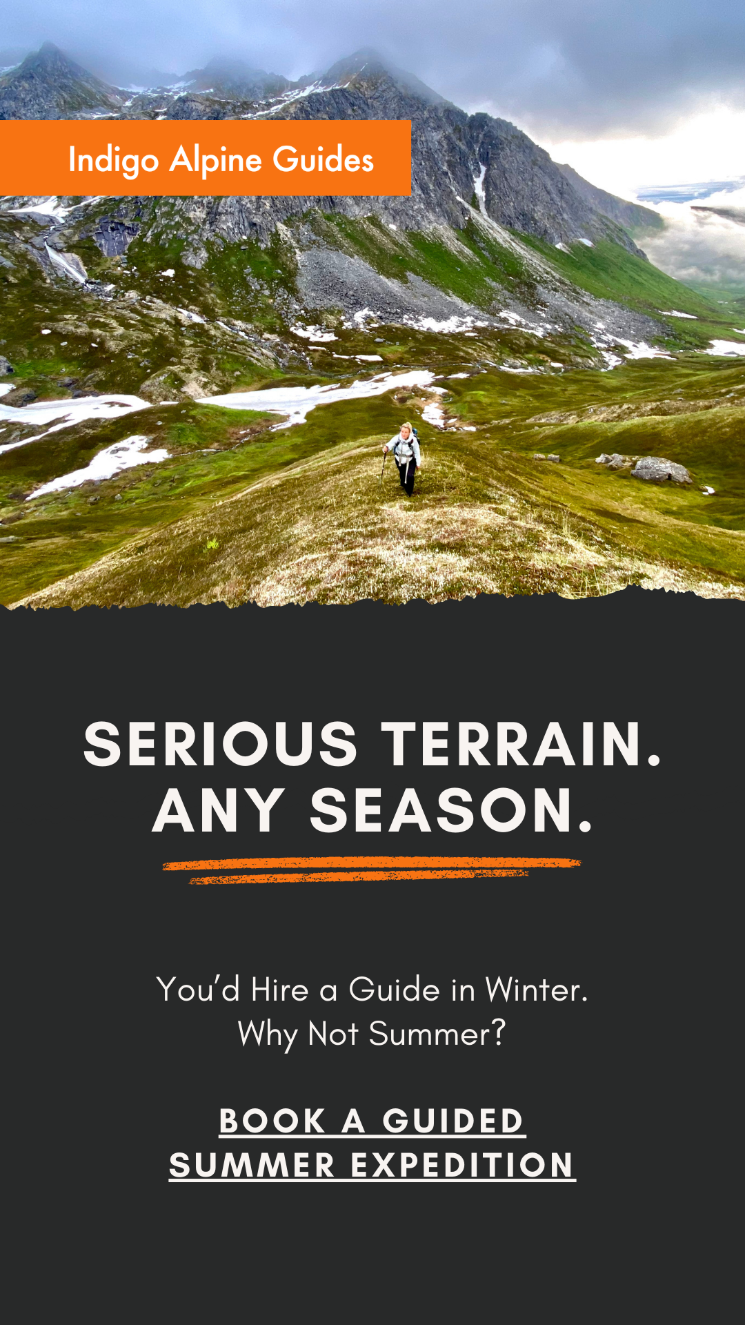 A hiker walking through a grassy mountain landscape with snow patches and steep rocky hills in the background, under a cloudy sky.