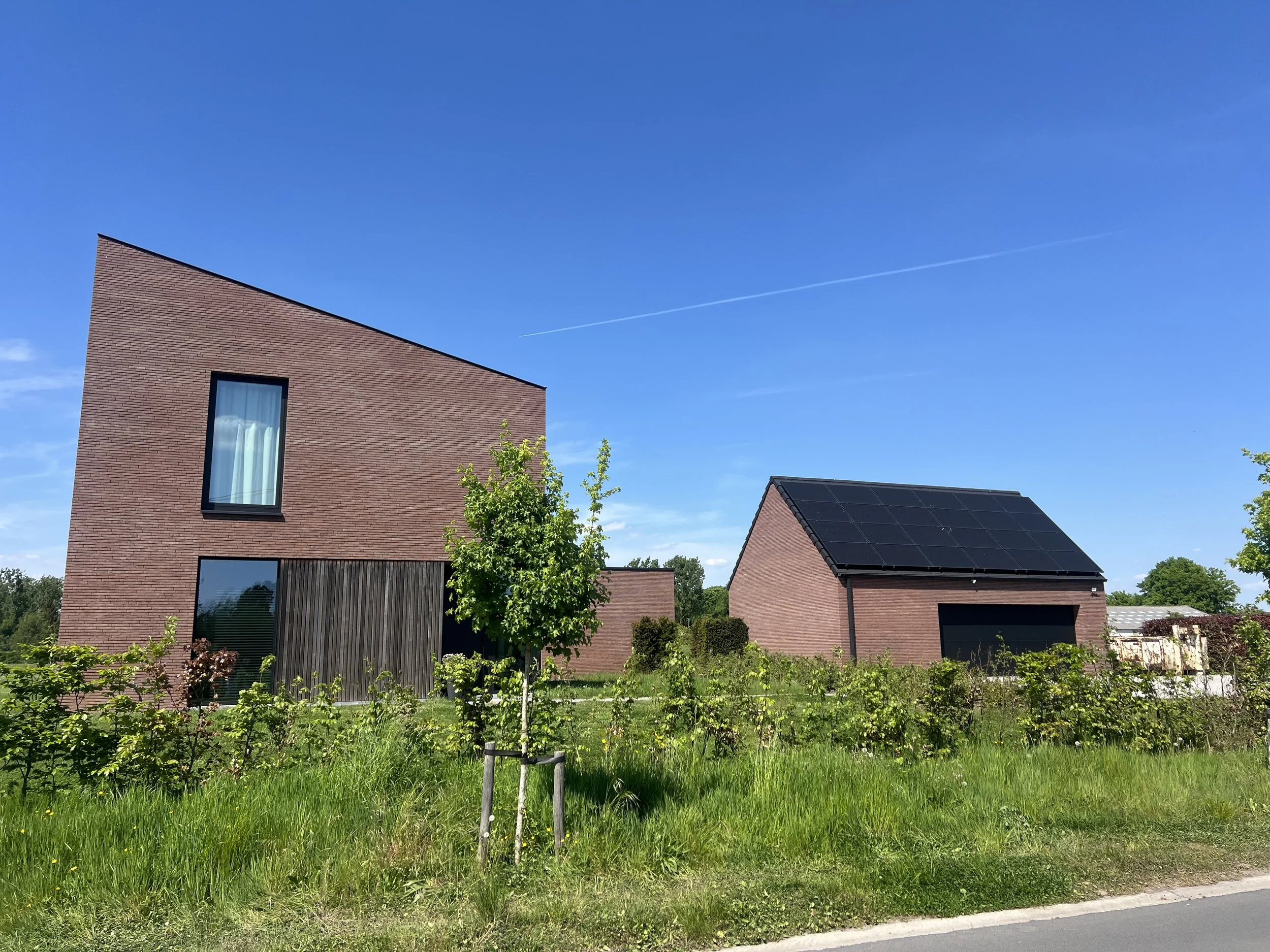 Residential area with modern brick houses, green trees, solar panels on the roof, and a clear blue sky.