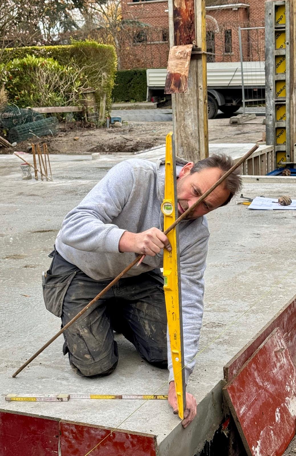 A man kneeling on a construction site, using a level to measure a concrete surface.
