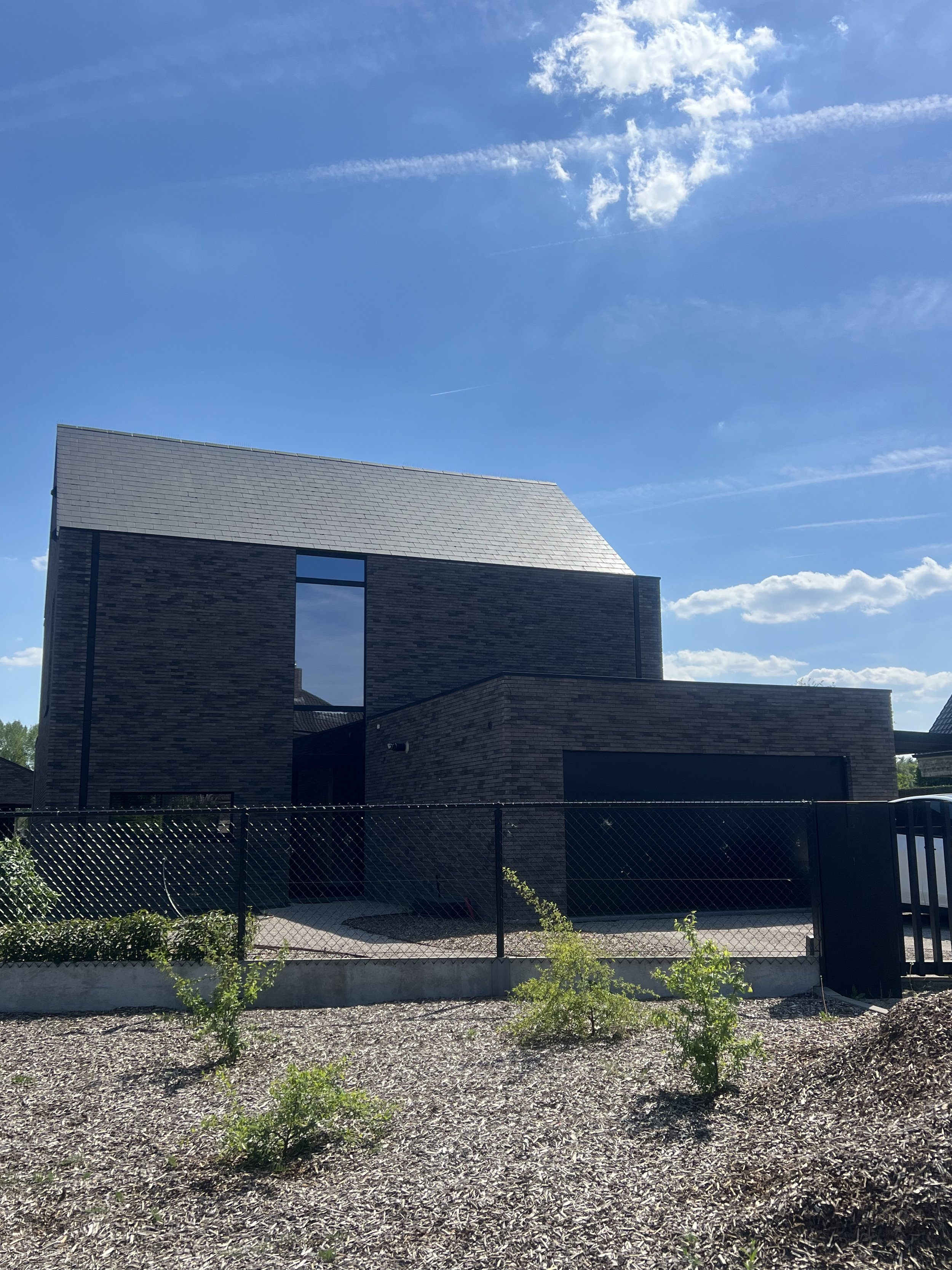 A modern brick house with a sloped roof and large windows, set against a bright blue sky with some clouds.