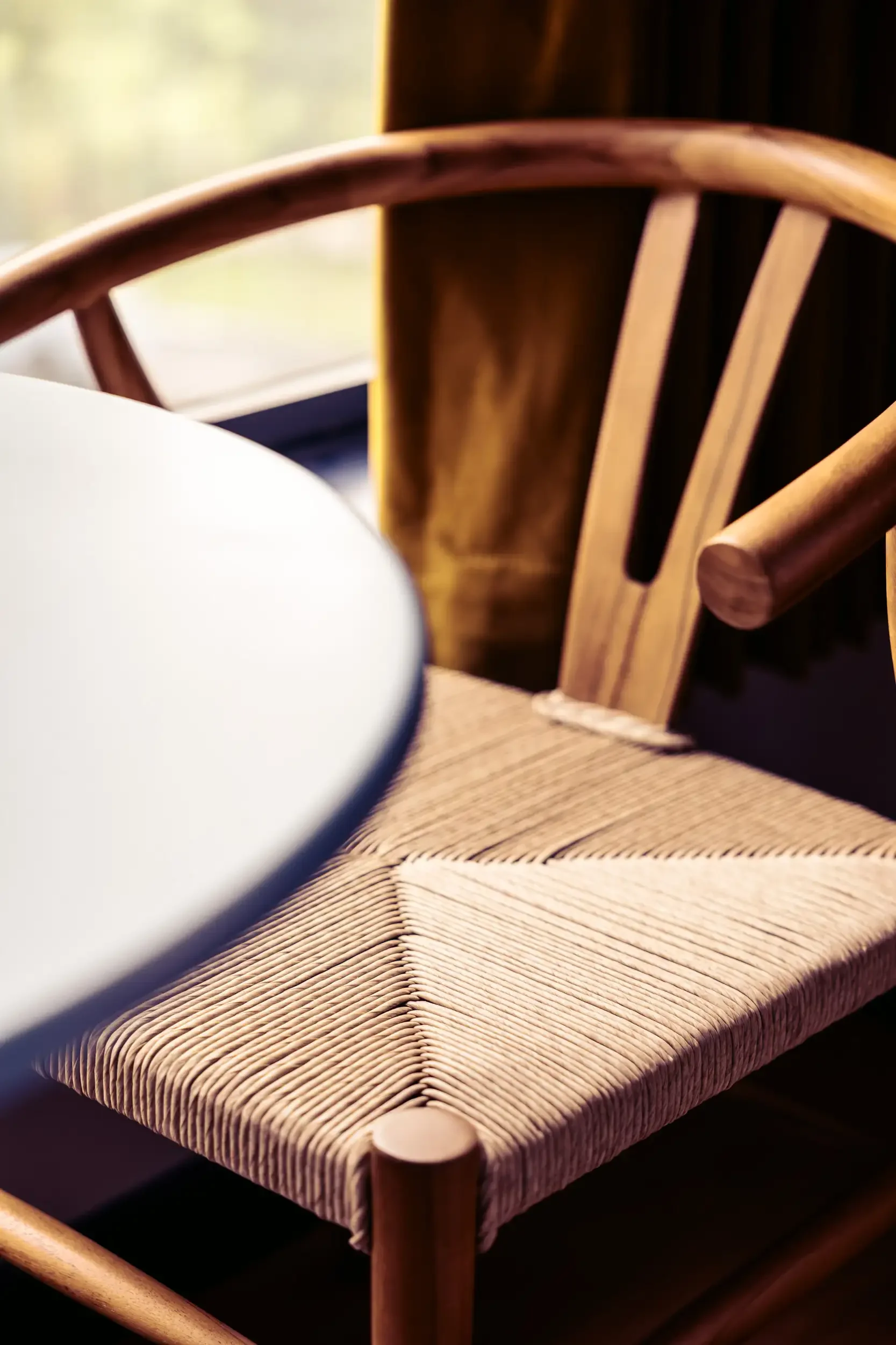 A wooden chair with a woven seat, next to a table in front of a window.