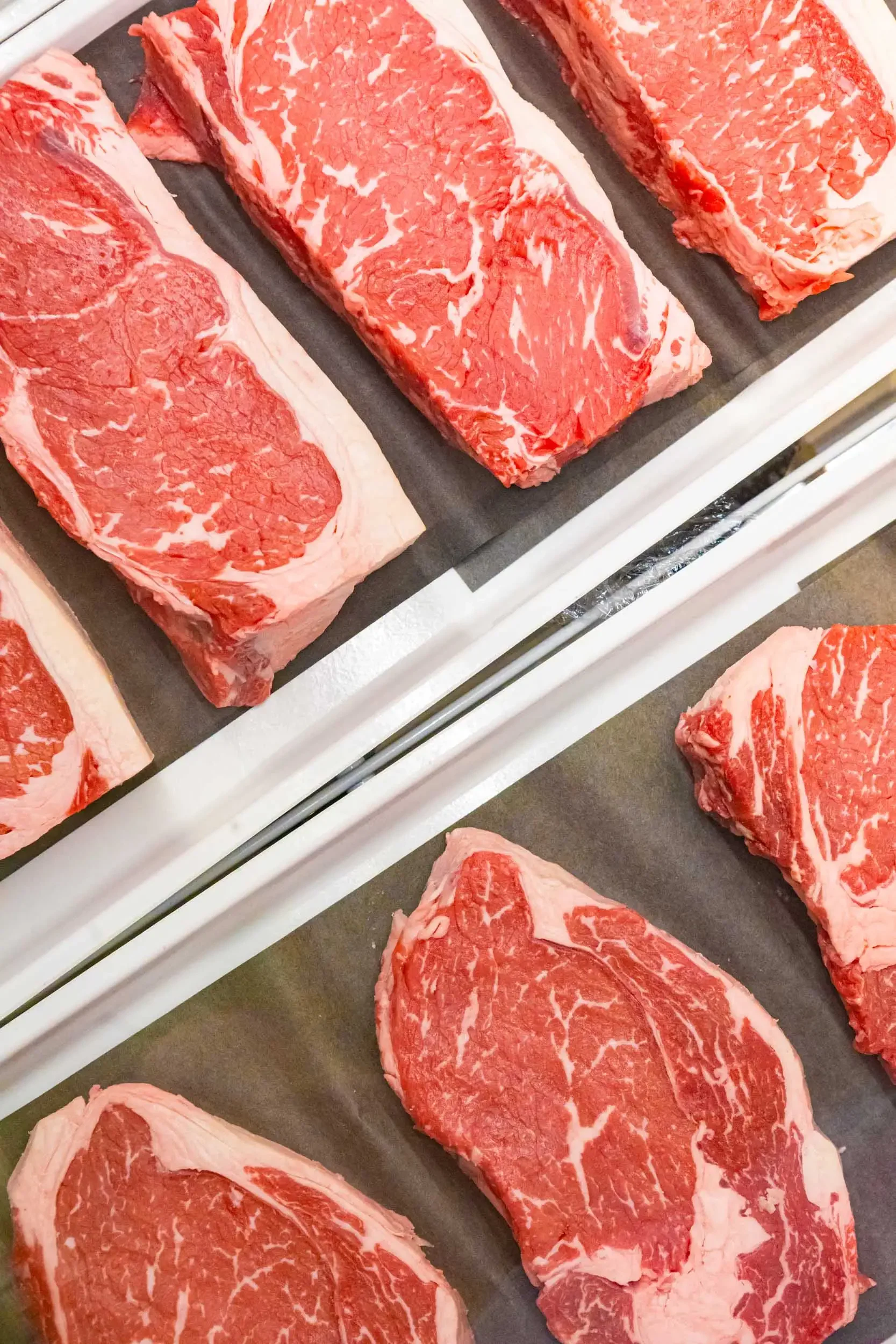 Several cuts of raw beef with marbling on display on a black tray.