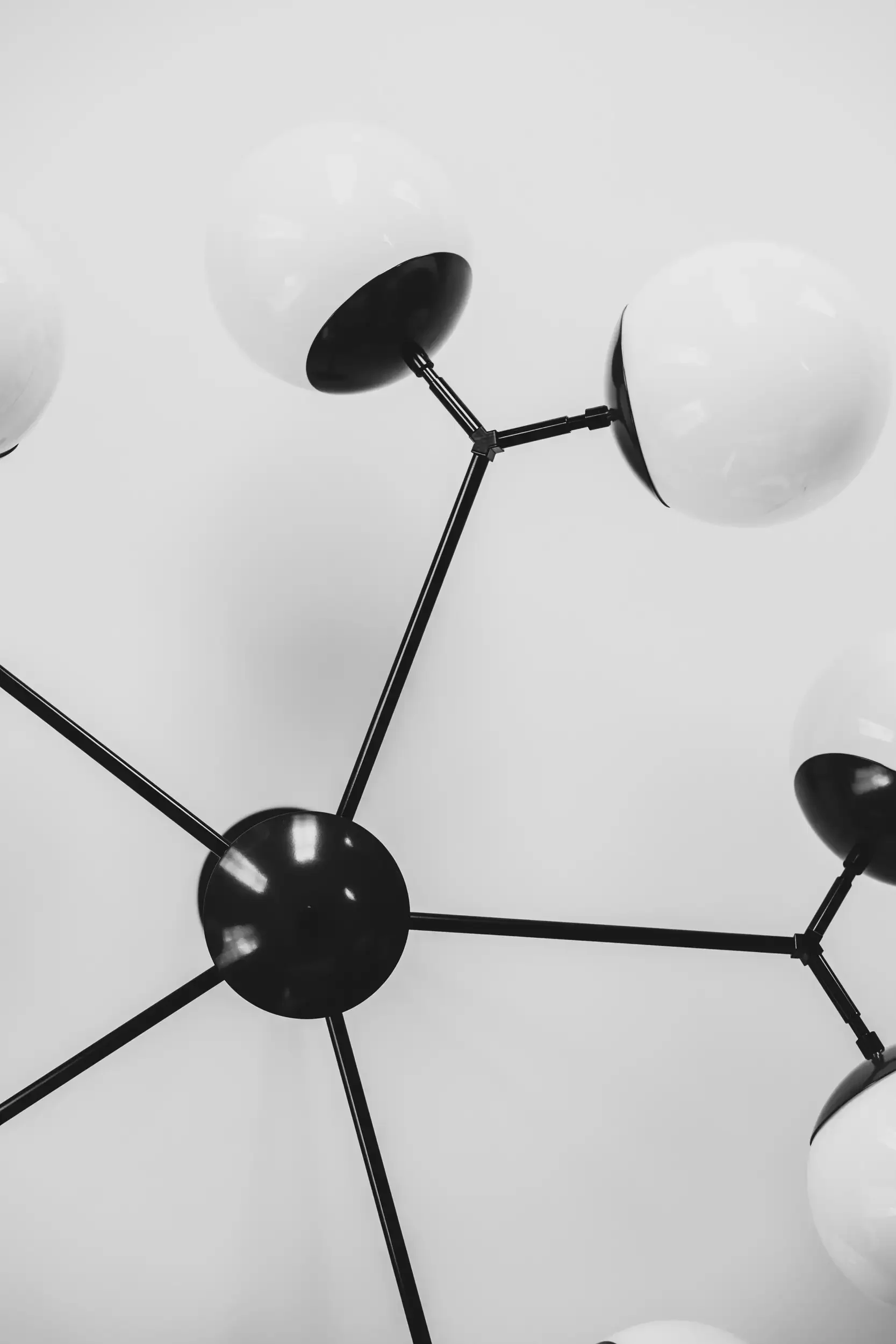 Black and white modern chandelier with spherical white bulbs attached to black rods and joints, viewed from below against a plain background.