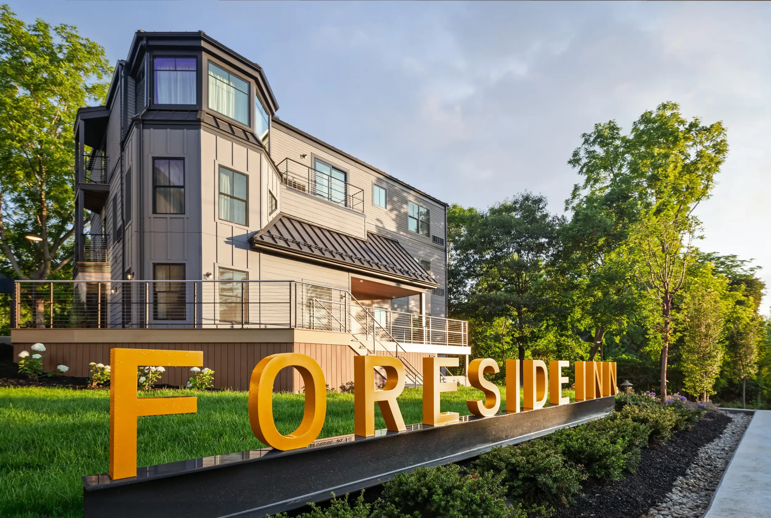 Modern multi-story apartment building behind a yellow sign spelling 'FOR RESIDEN' in large letters, with trees and a grassy area in front.