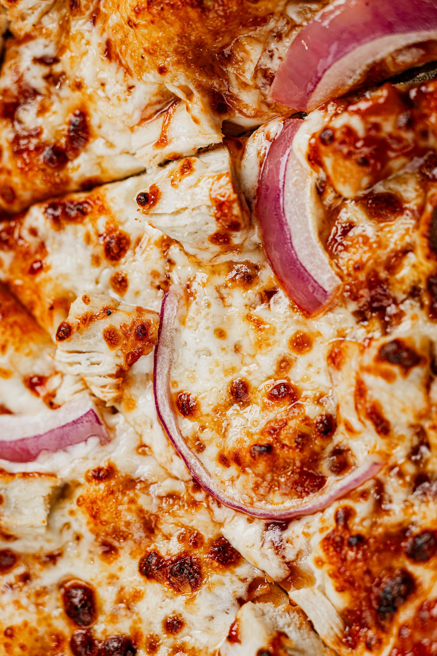 Close-up of a cooked pizza topped with red onion slices, chicken pieces, melted cheese, and tomato sauce.