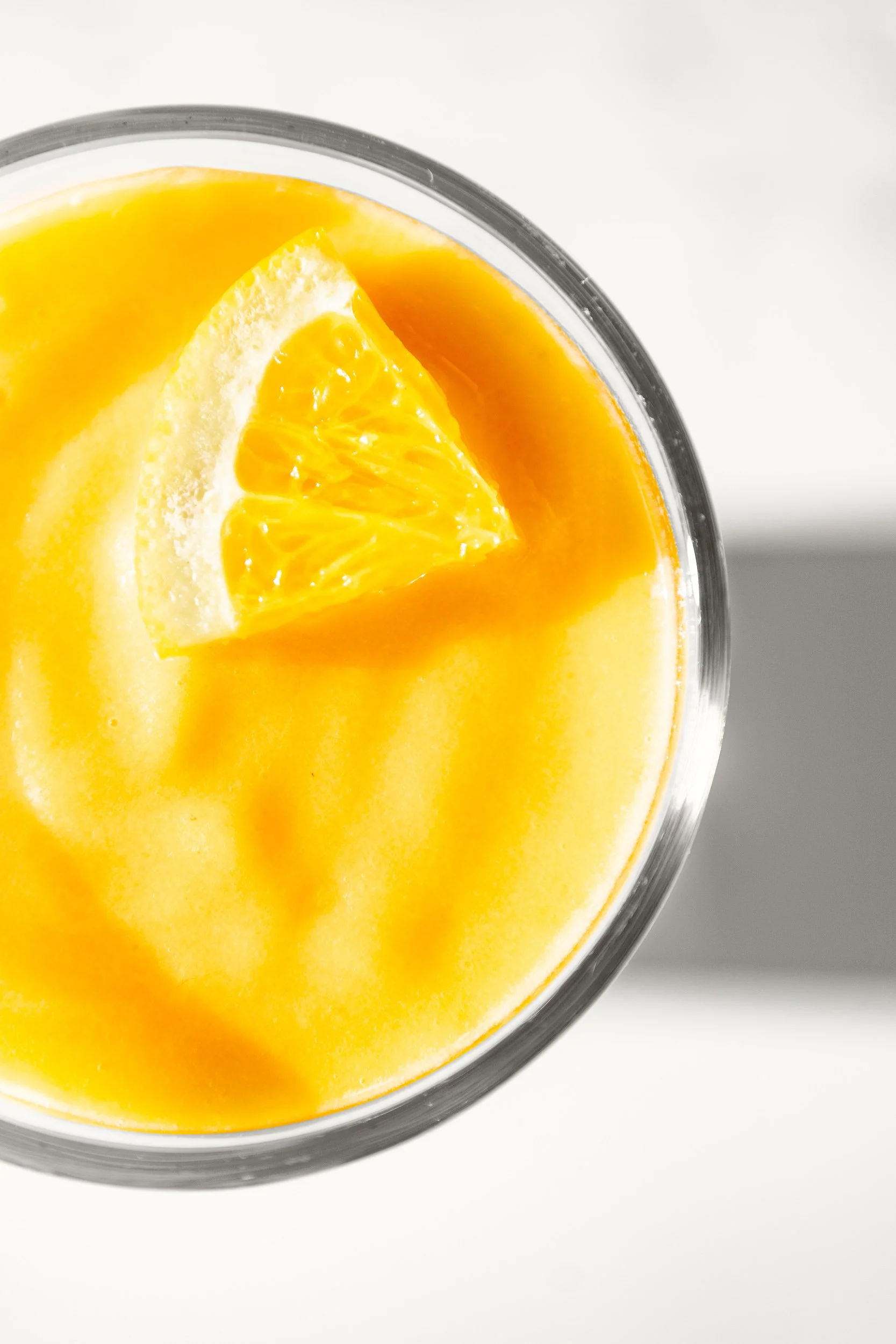 Top view of a glass of orange juice with an orange wedge garnish.