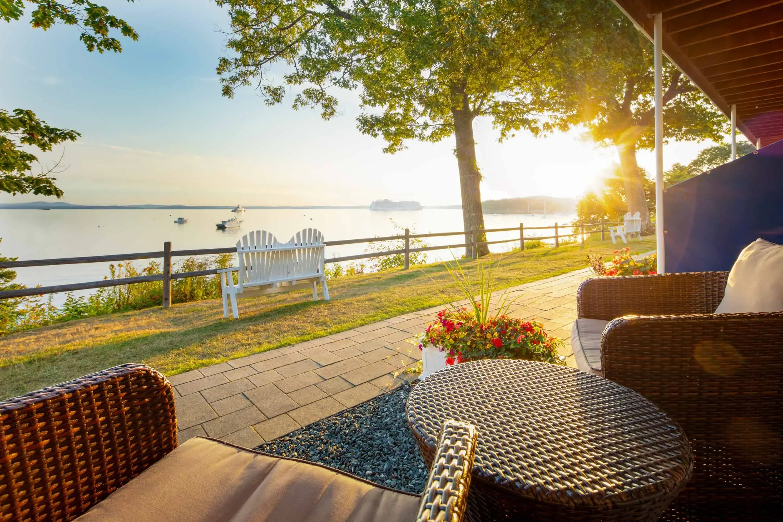 Seating area on a patio overlooking a lake with boats, trees, and a setting sun.