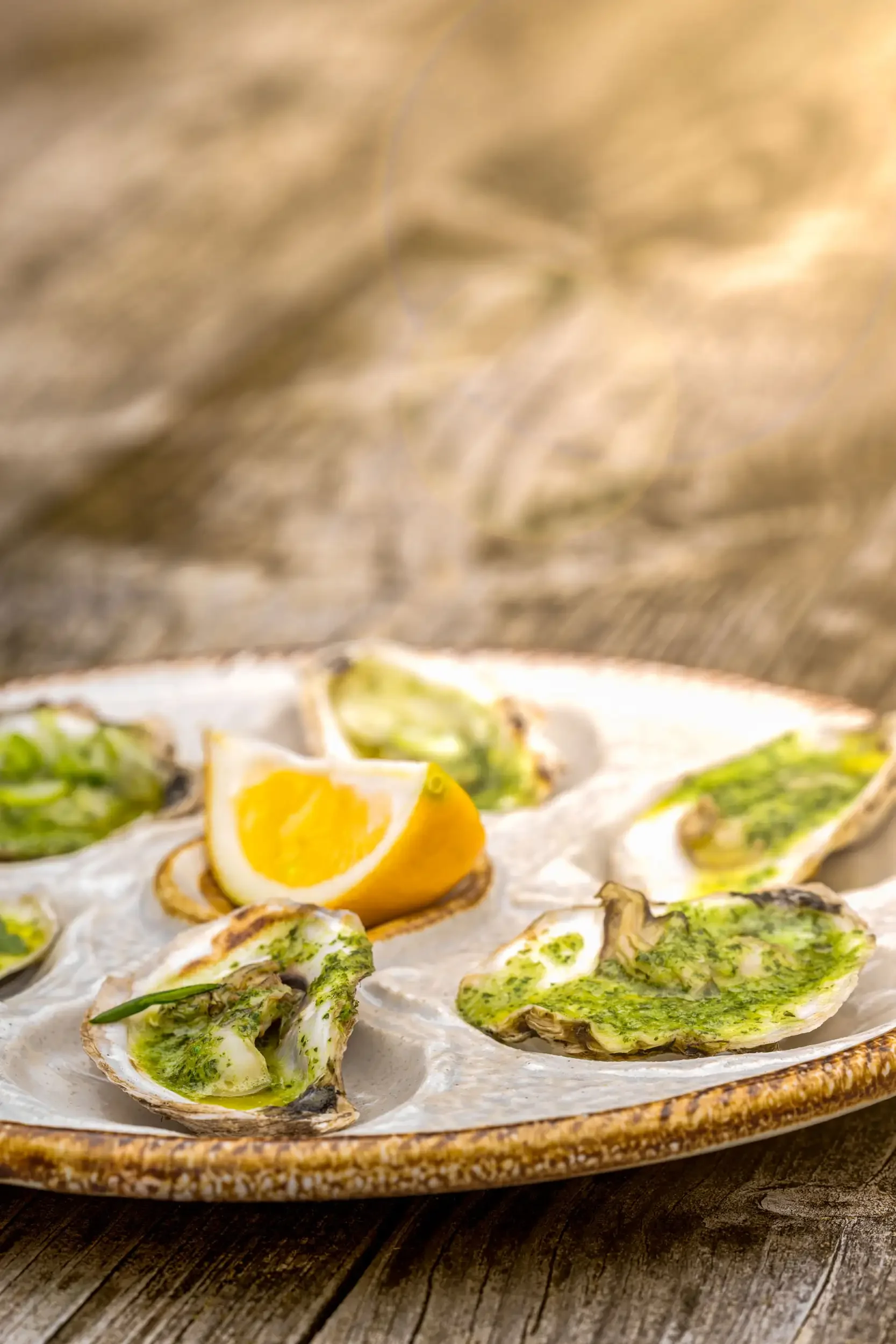 A ceramic plate of grilled oysters topped with green herbs, garnished with lemon wedges.