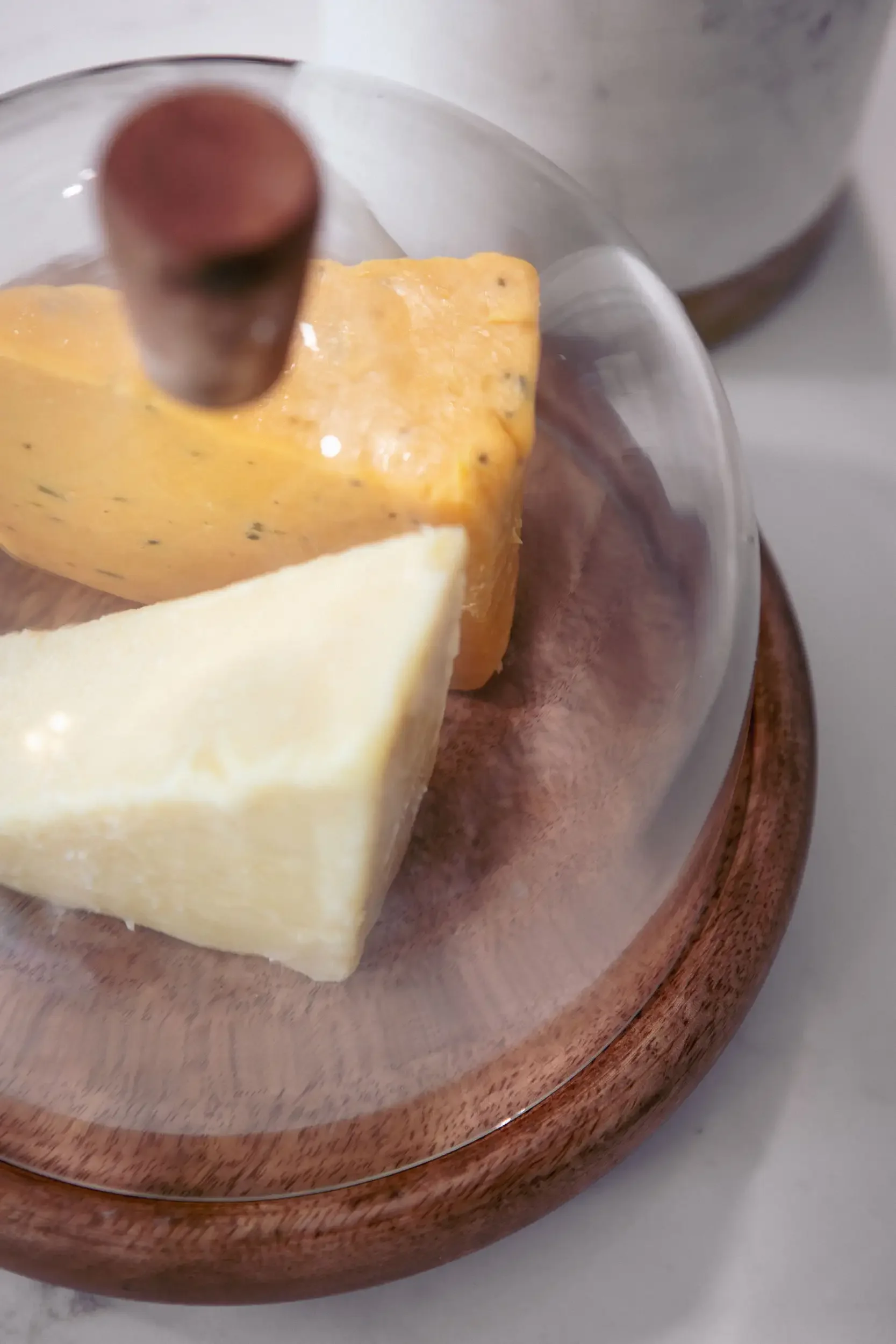 Close-up of a glass dome covering pieces of cheese on a wooden serving tray.