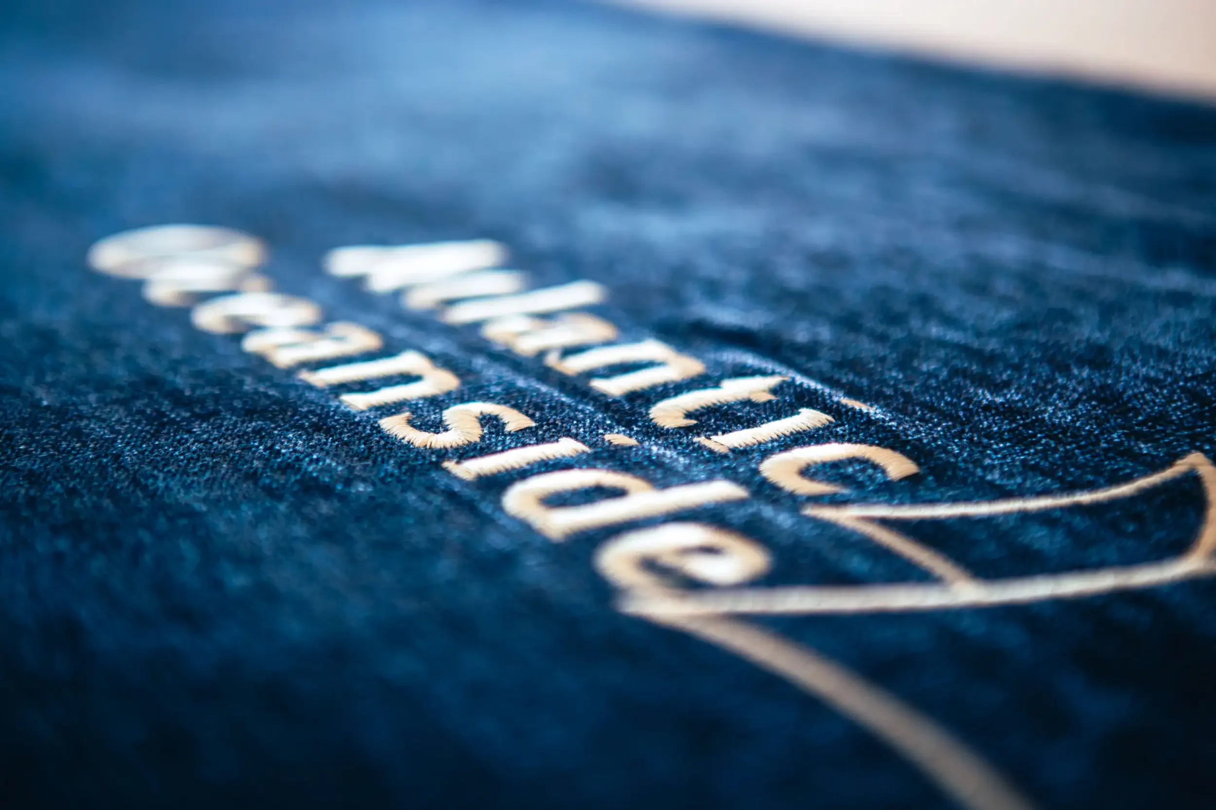 Close-up of a blue fabric with embroidered white text, blurred in the background.