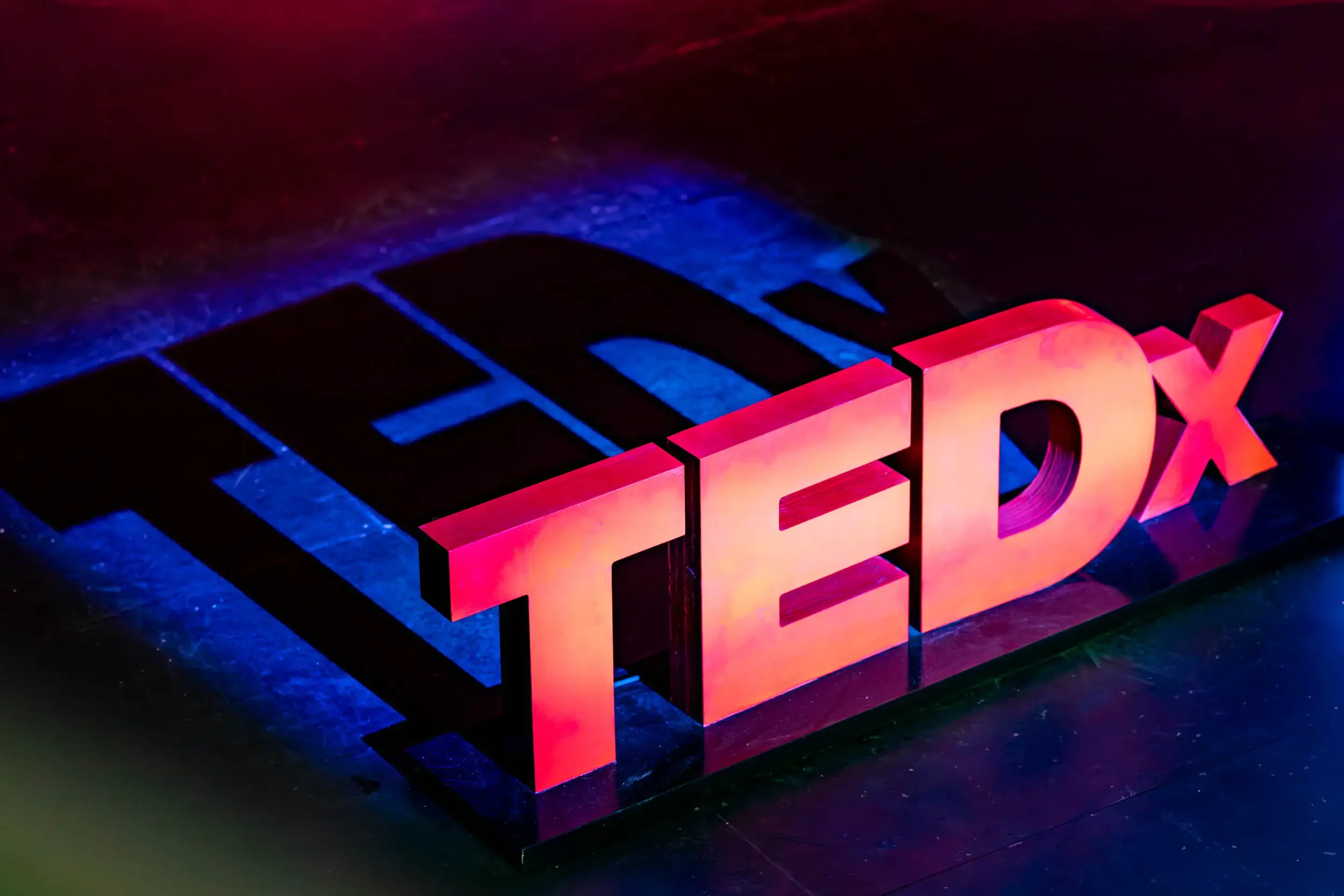Close-up of the Fox Corporation logo illuminated in pink and red lights on a dark surface.