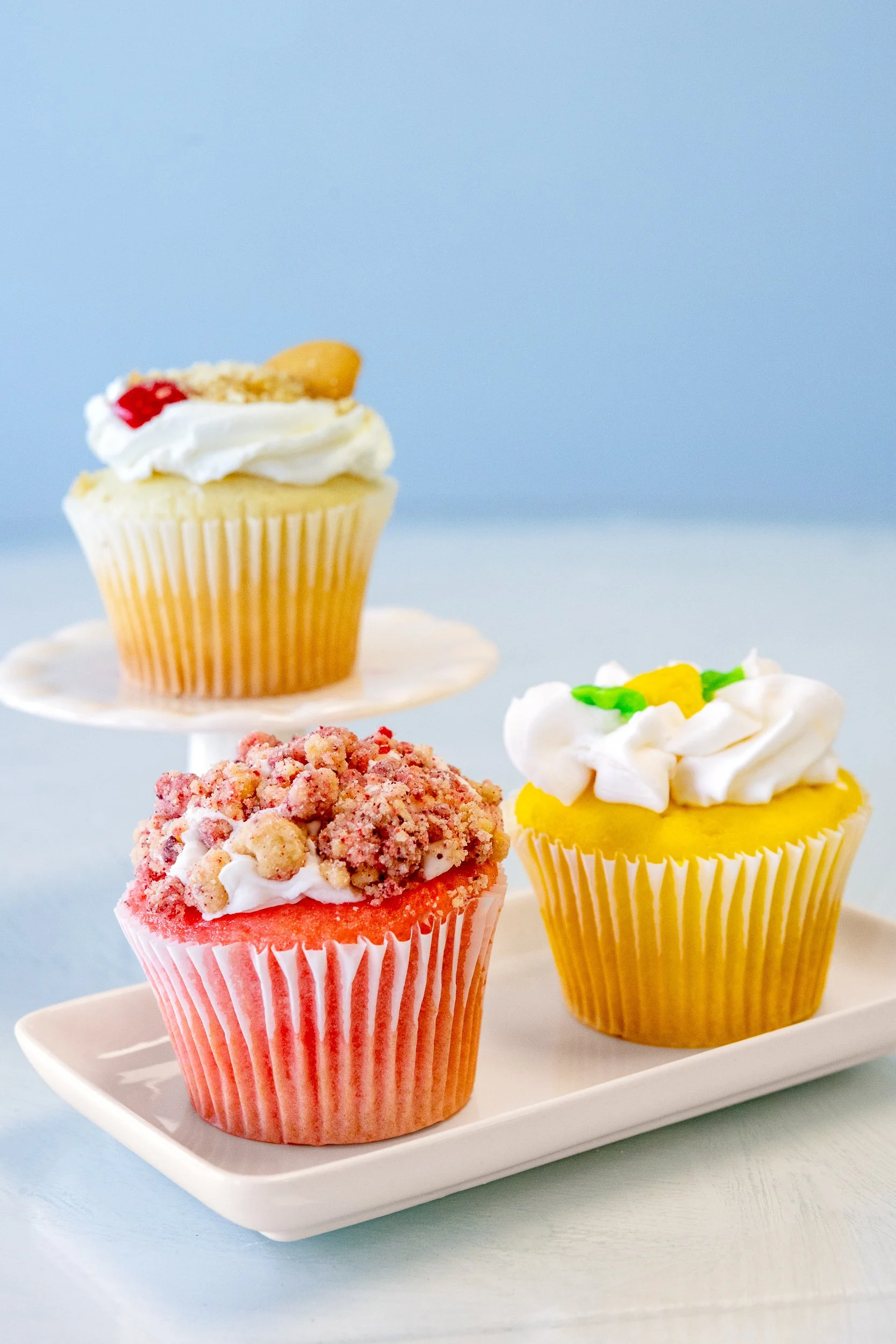 Three decorated cupcakes on a white rectangular tray, with a light blue background.