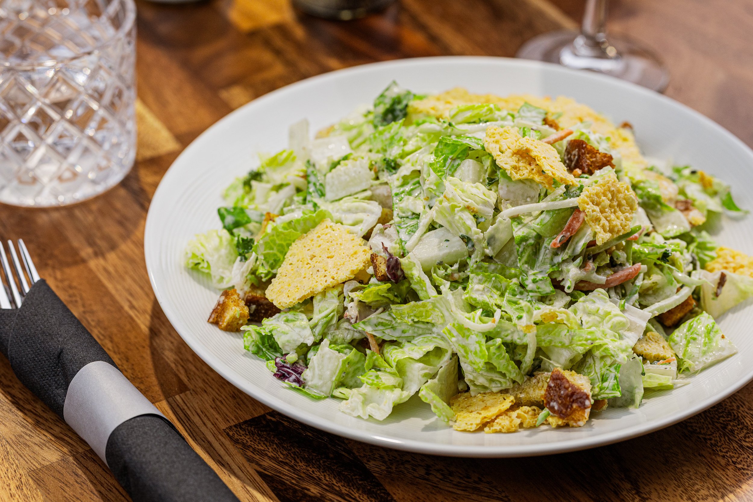 A plate of Caesar salad with romaine lettuce, croutons, grated cheese, and Caesar dressing on a wooden table.