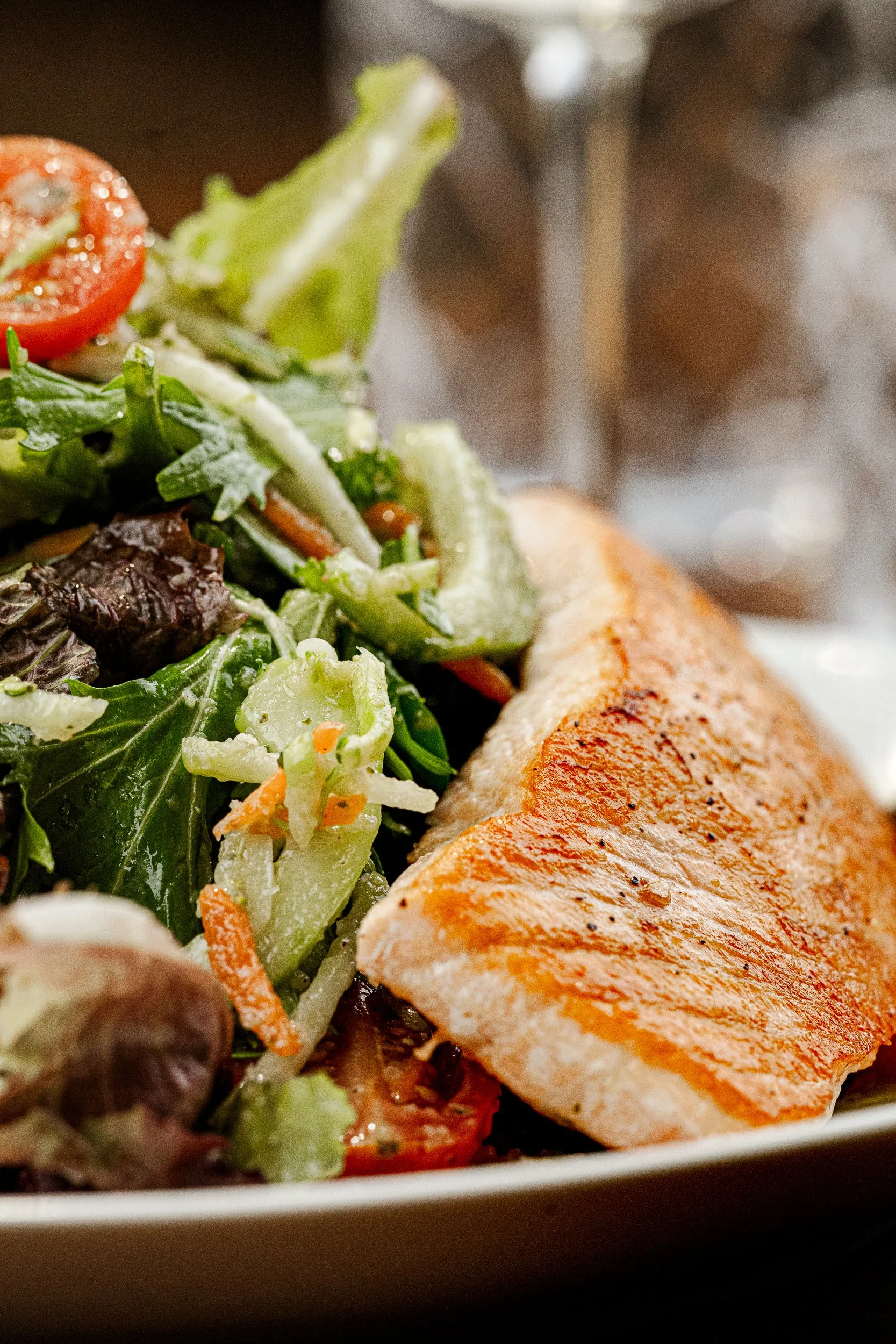 Close-up of a grilled salmon fillet served with a mixed green salad including cherry tomatoes, cucumbers, and shredded carrots.