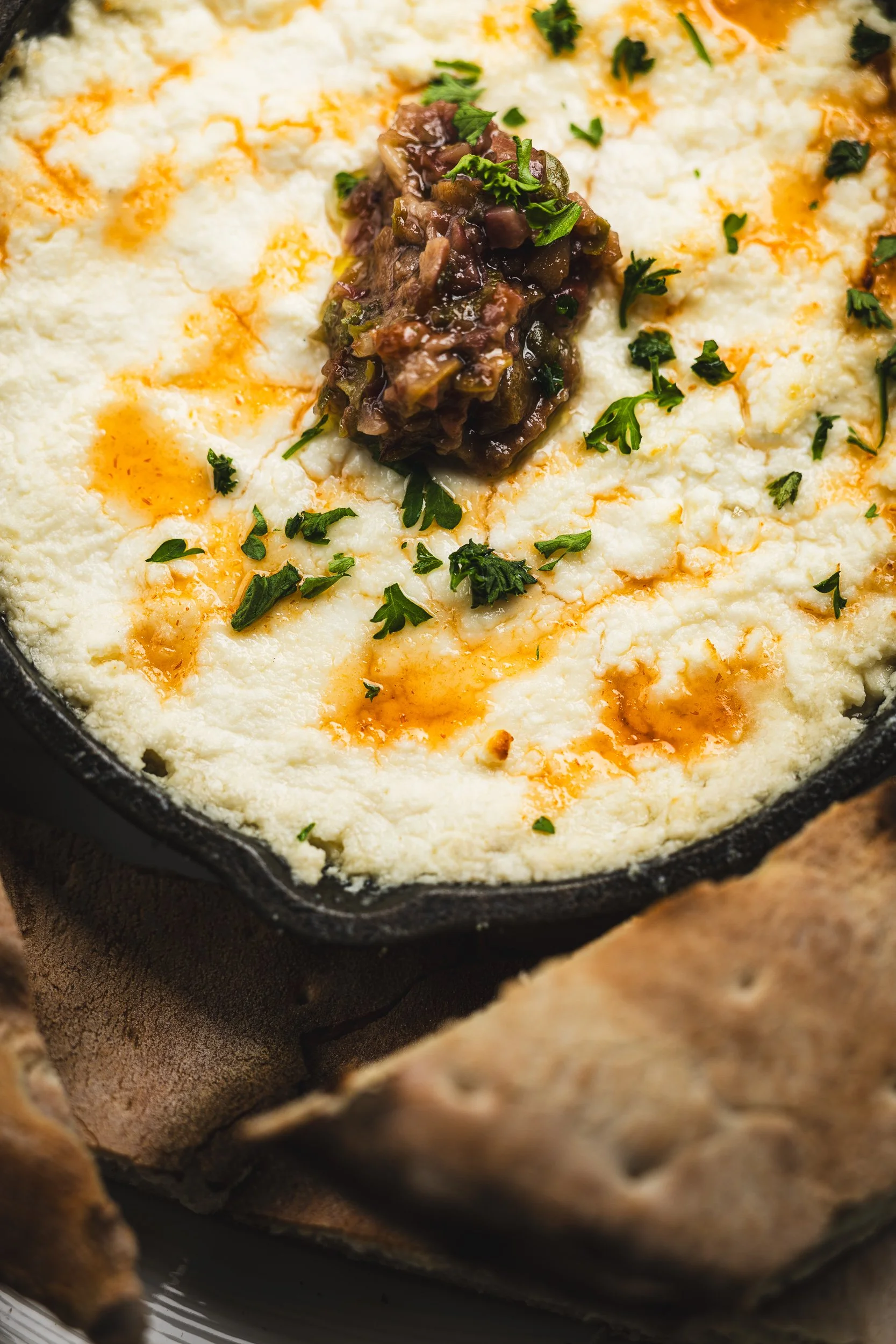 A cast iron skillet containing mashed potatoes topped with gravy, chopped parsley, and a dollop of mushroom gravy, served with pita bread on a plate.
