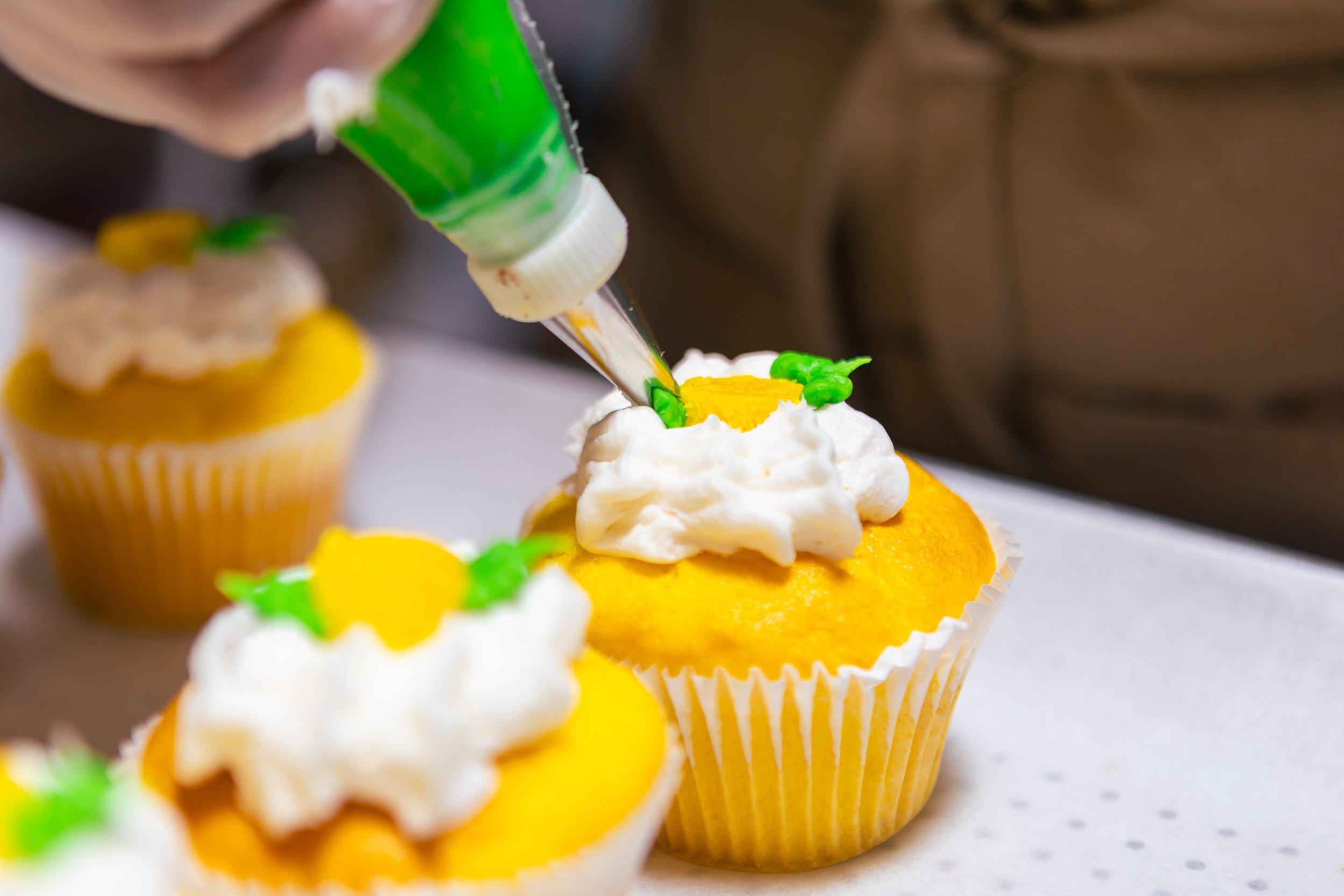 A cupcake being decorated with green and yellow icing using a piping bag filled with green icing.