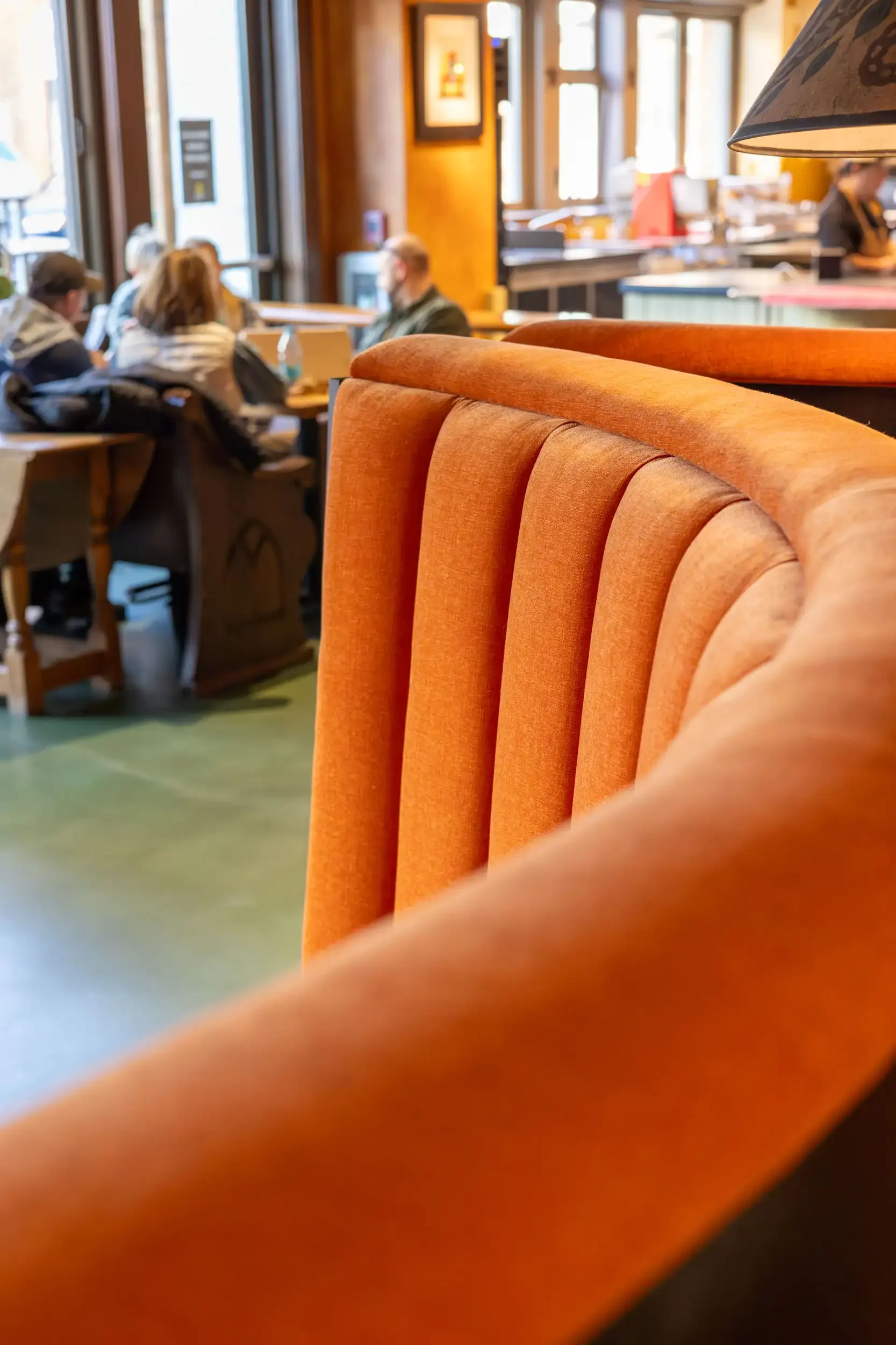 Close-up of an orange upholstered seat or booth in a restaurant with people dining in the background, blurred.