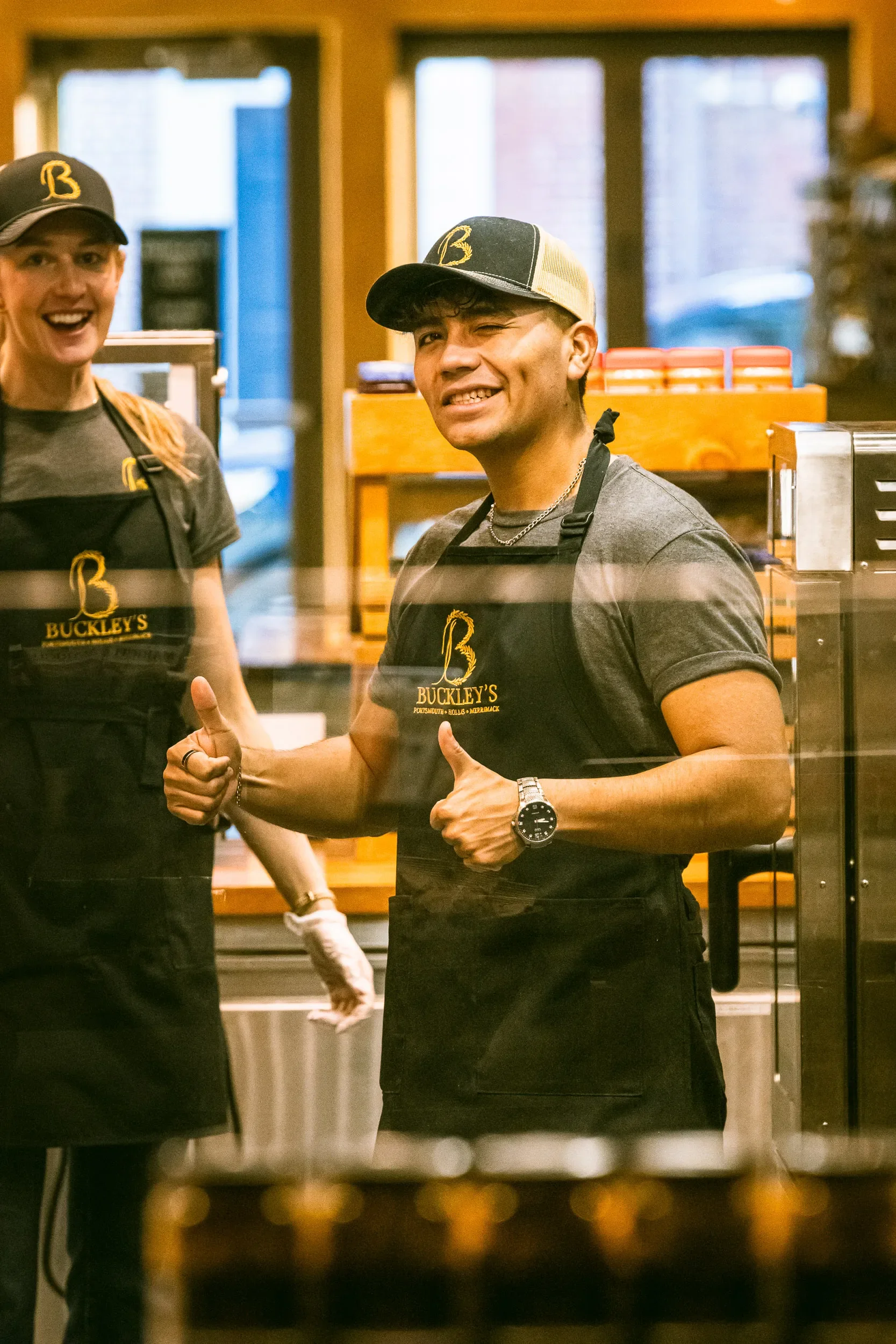 Photo of two smiling staff members inside Buckley's restaurant, wearing black aprons and caps with the Buckley's logo, giving thumbs up.
