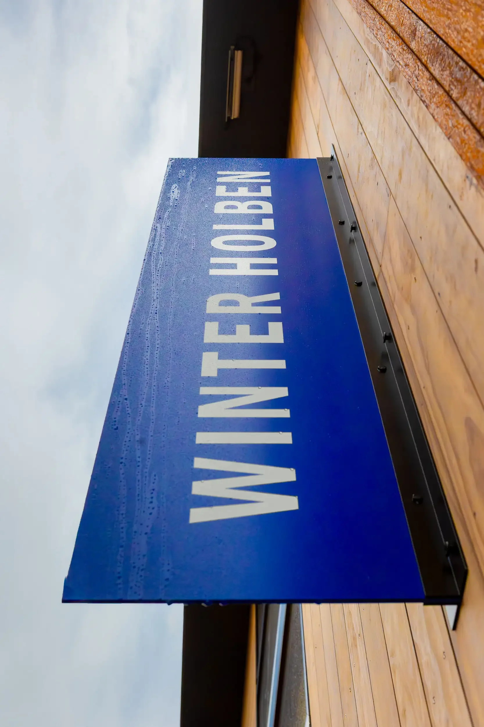 Blue sign with white text that says "WATER HABO" on a wooden surface next to a cloudy sky.