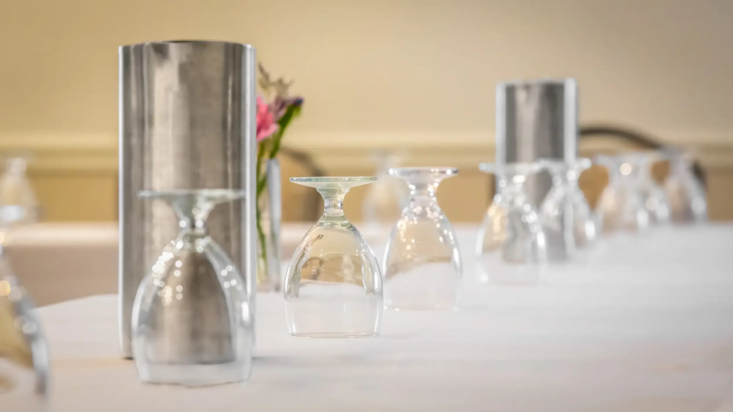 Upside-down wine glasses and a floral arrangement on a table, with blurred background.