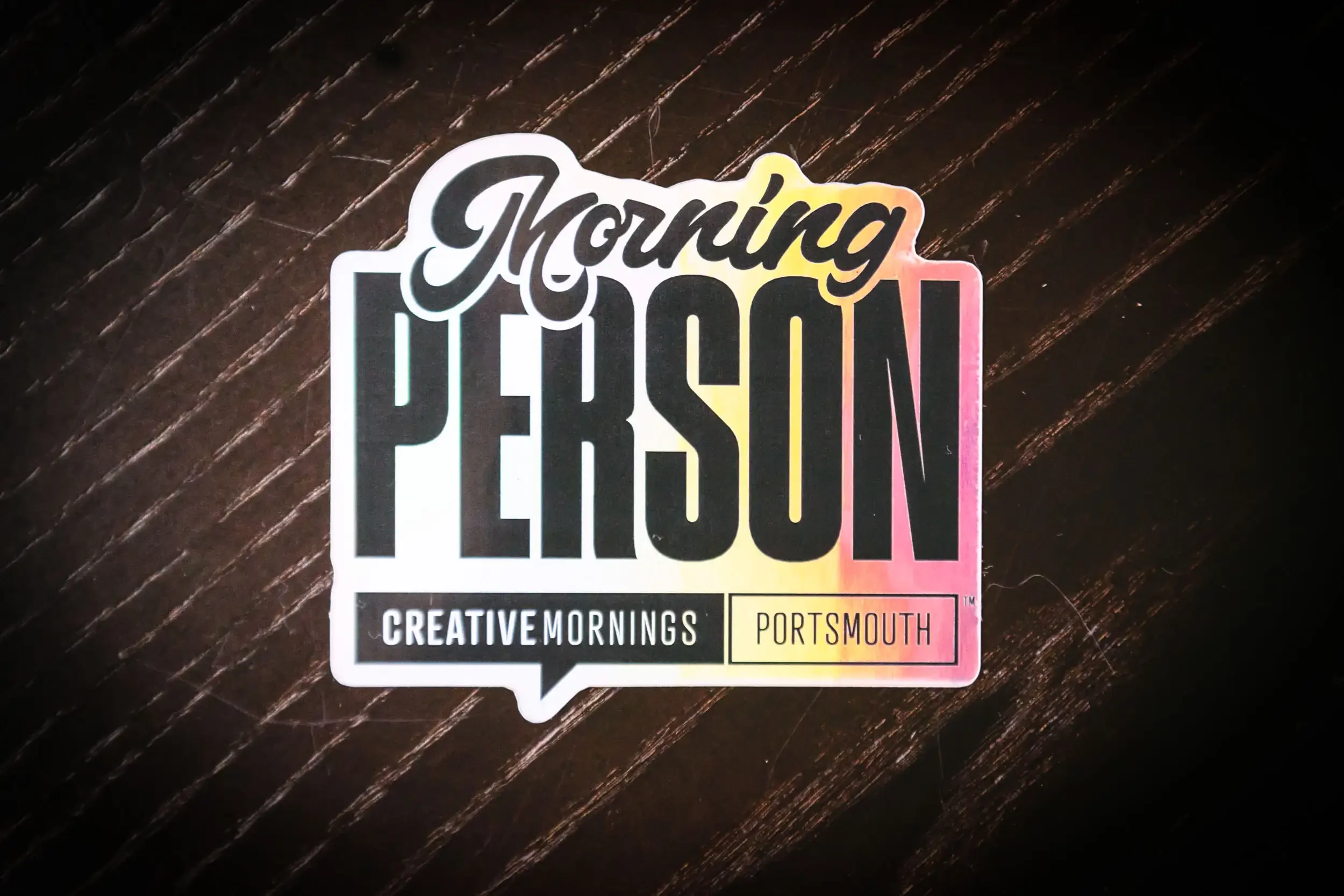 Sticker with text reading 'Thriving Passion Creative Mornings Portsmouth' on a dark wooden surface.