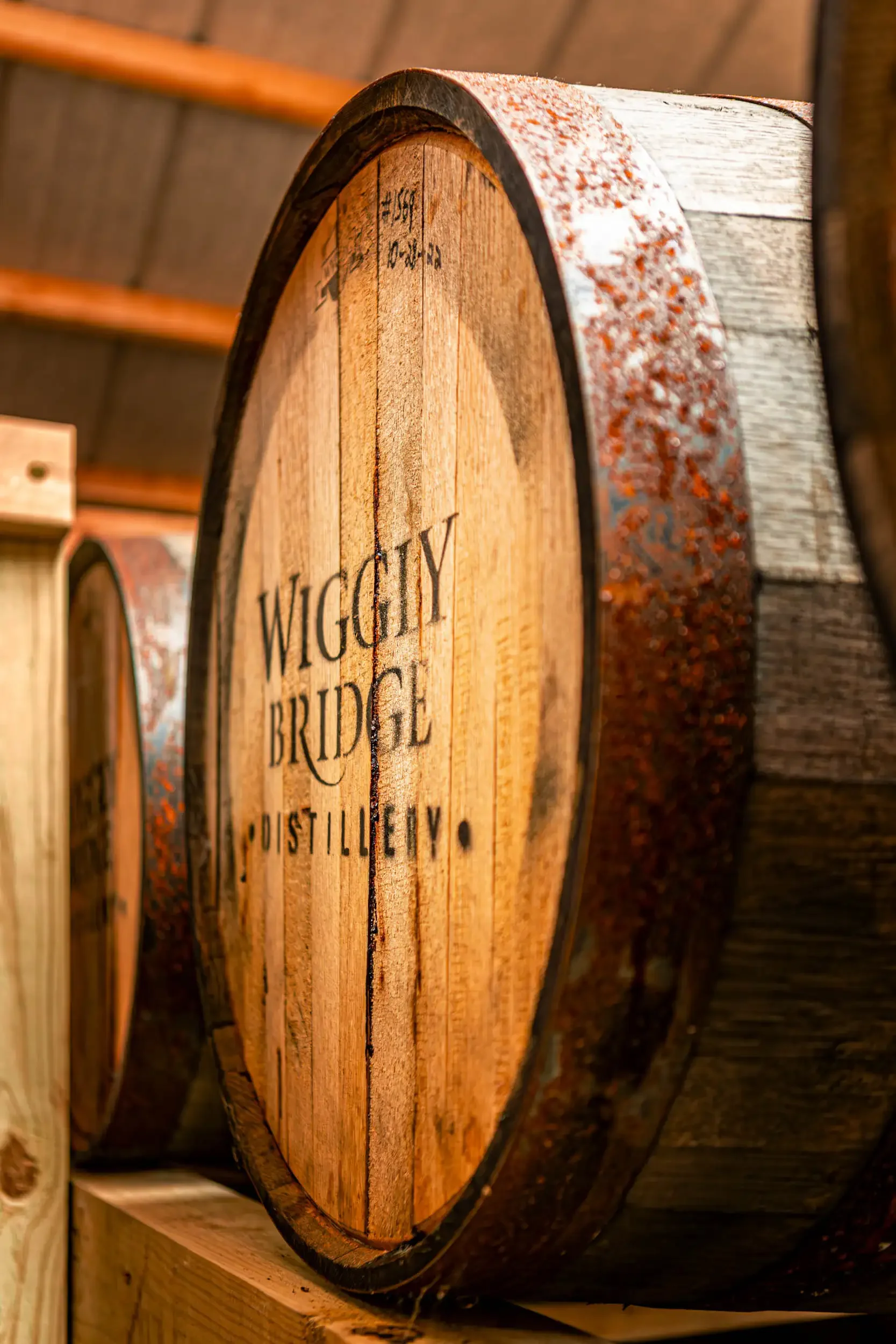 Close-up of a wooden barrel with the words "WIGUIY BRIDGE DISTILLERY" written on the front, inside a rustic setting.