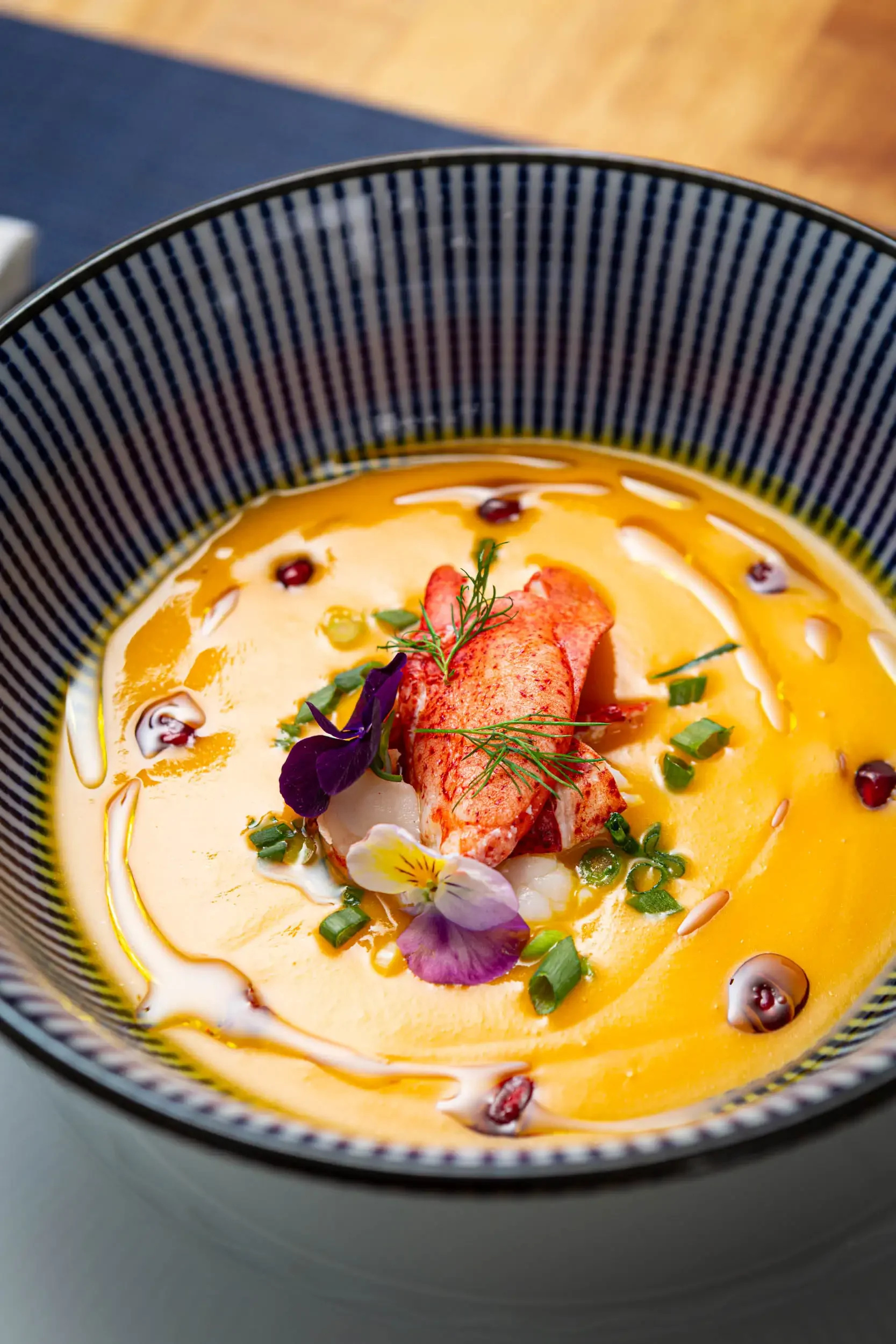 Close-up of a bowl of creamy yellow soup garnished with herbs, edible flowers, and pomegranate seeds.